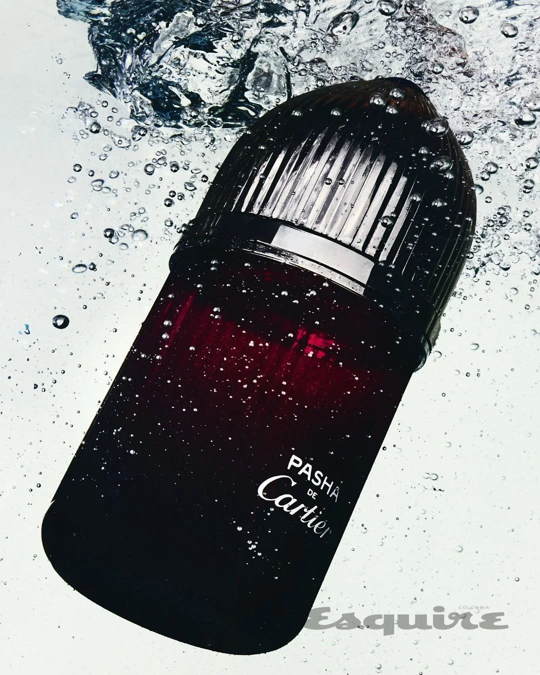 A botella de perfume llamada 'Pasión' de Cartier, sumergida en agua con burbujas, vista en ángulo invertido.