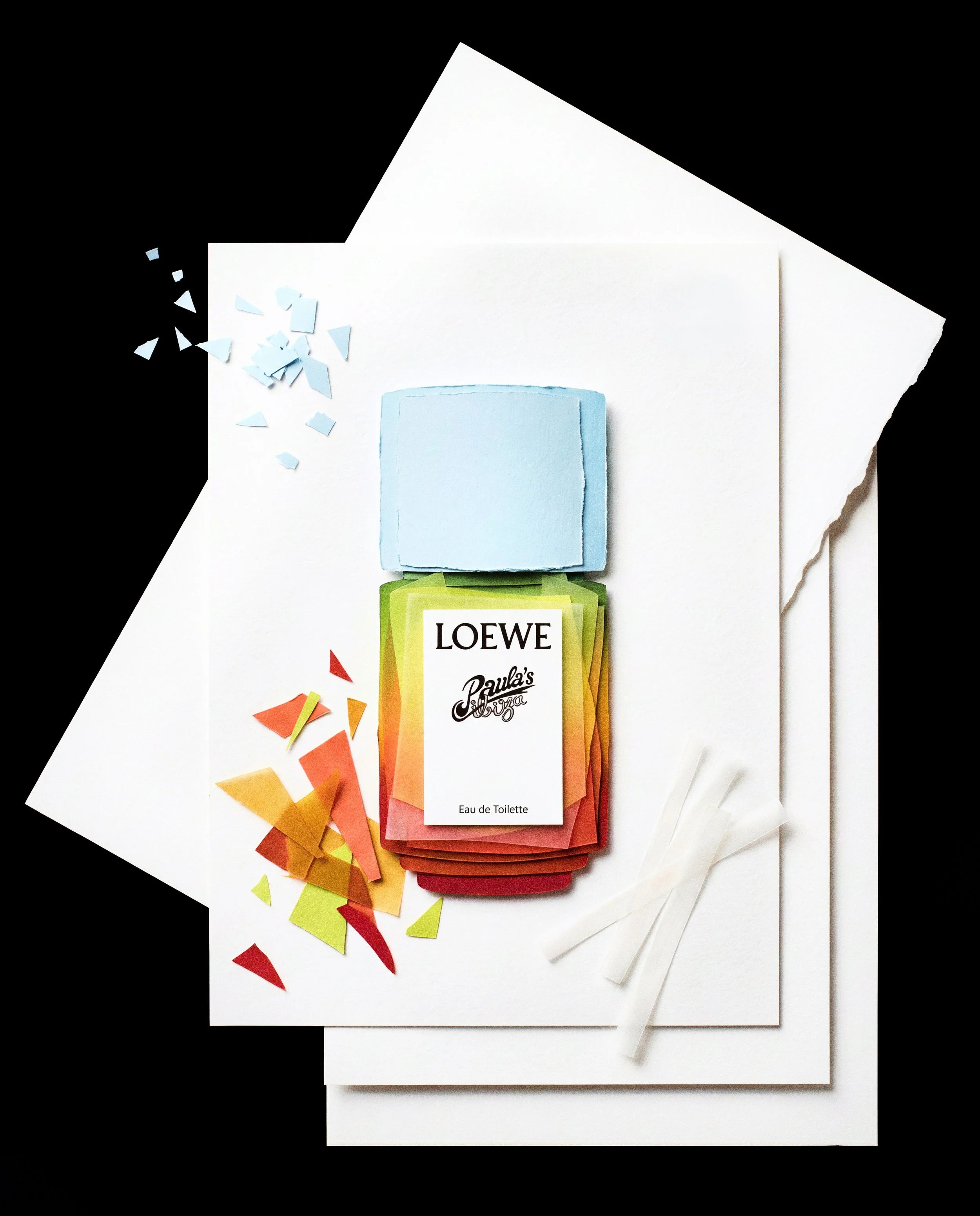 Paquete de perfume Loewe Paula's Ibiza con envoltorio de papel de colores amarillo, naranja y rojo, con confeti de colores y papel cortado en blanco y azul