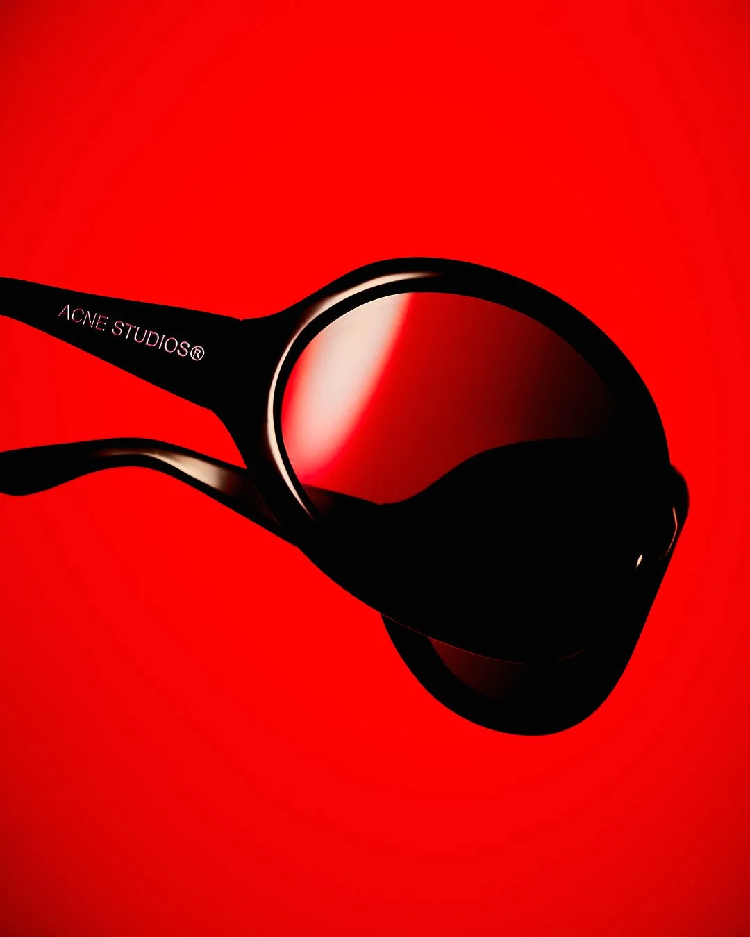 Gafas de sol de color negro con lentes rojos, sobre fondo rojo.