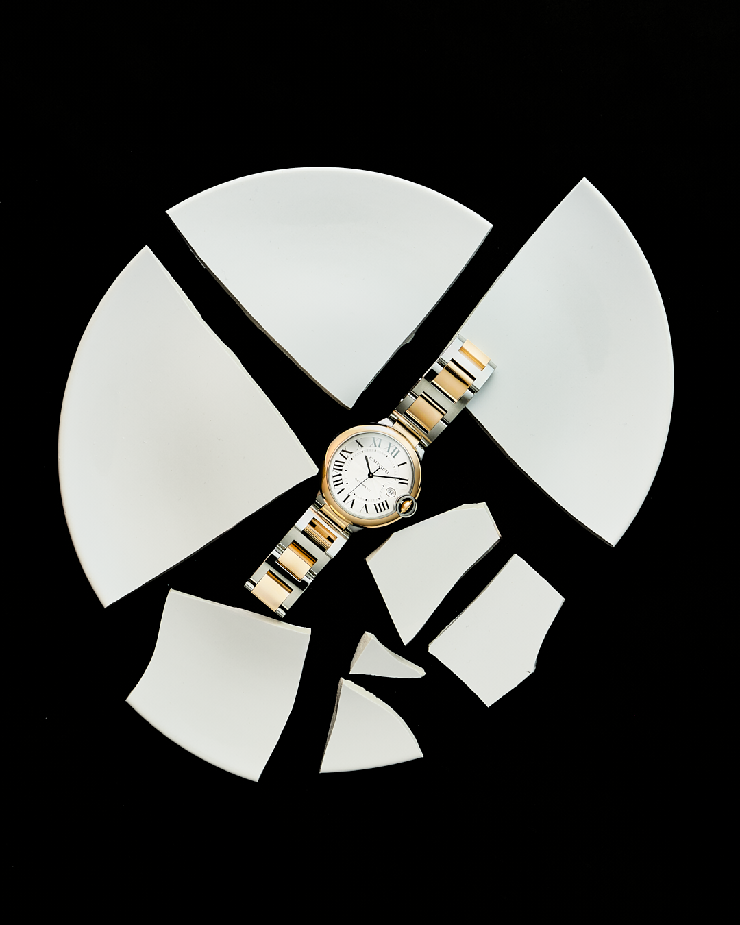 Reloj de pulsera de oro y plata sobre piezas blancas en forma de círculo roto en fondo negro.