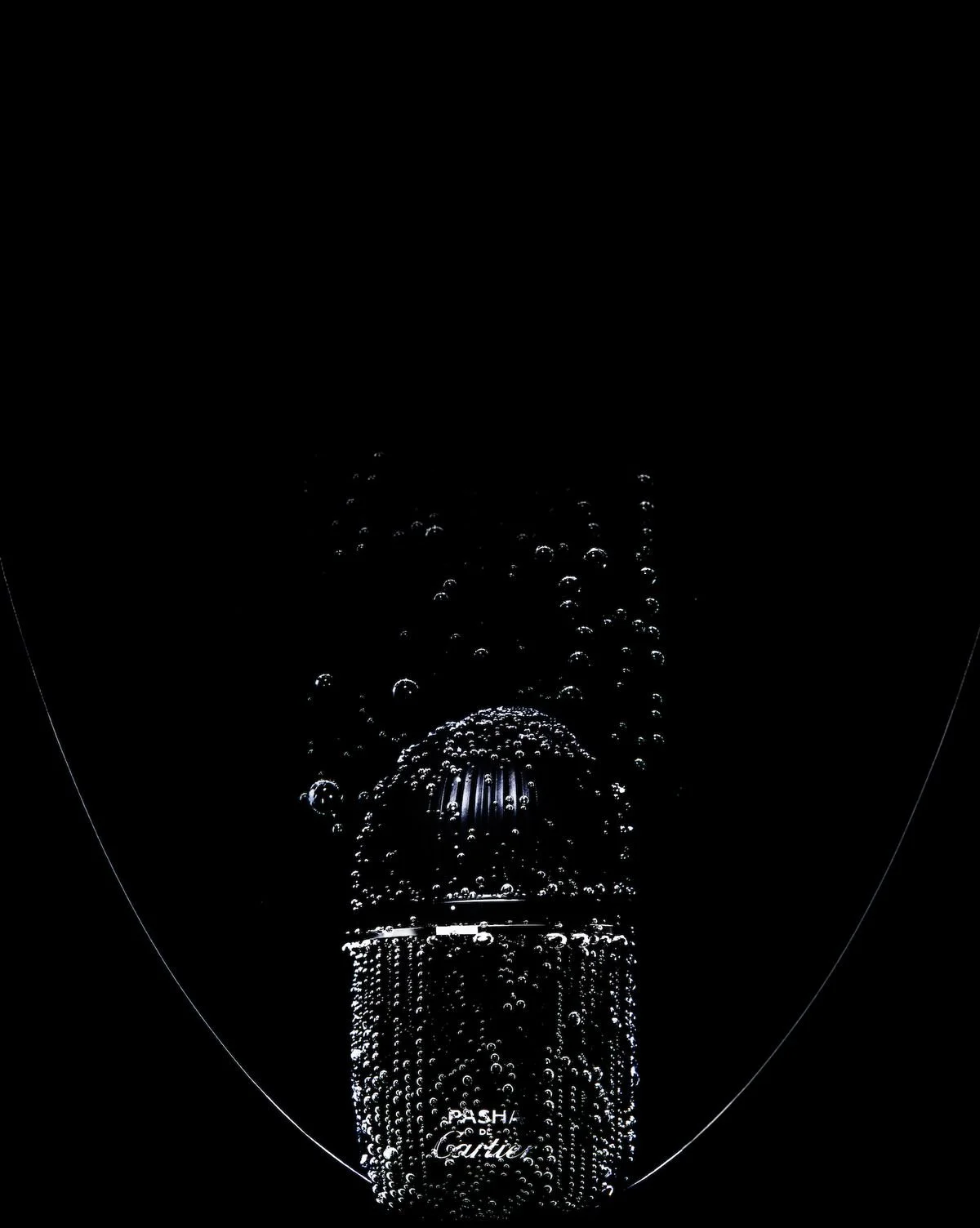 Fotografía en la oscuridad de una botella de perfume con burbujas de agua en el aire.