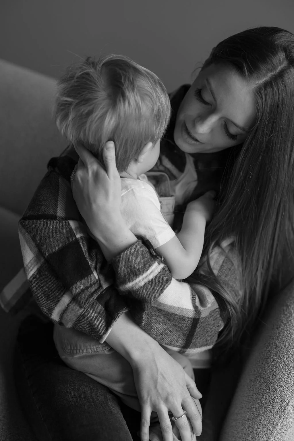 A woman with long hair and a young boy in a plaid shirt sharing an affectionate moment, hugging tightly.