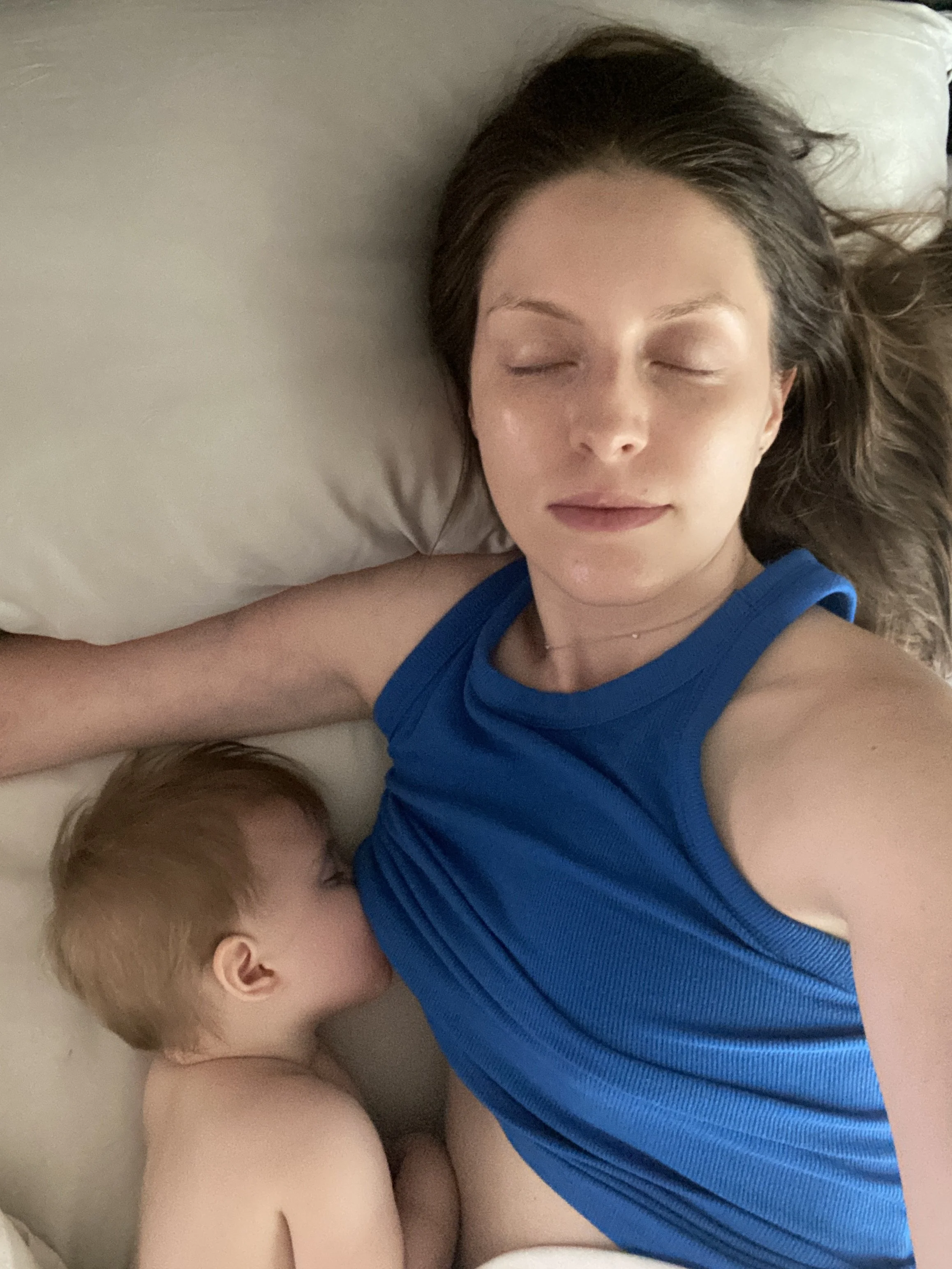 A young woman sleeping while her baby sleeps and nurses next to her.