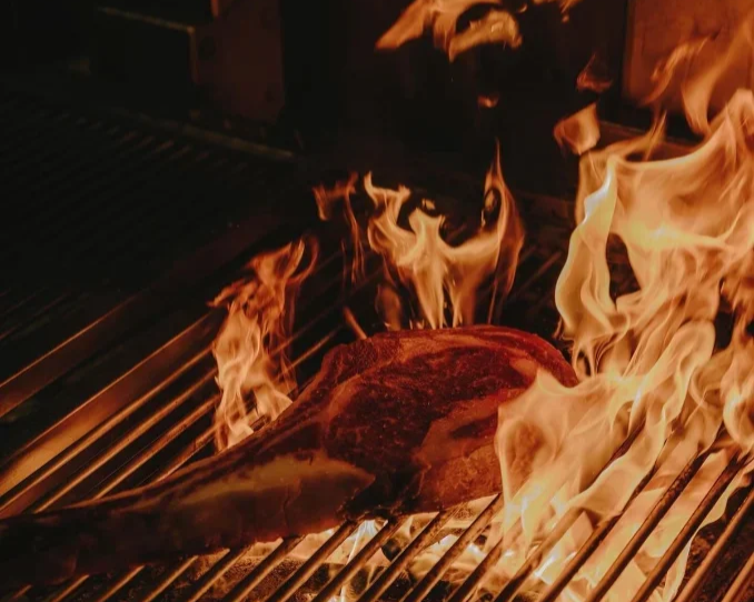 A piece of meat on a grill with flames around it.