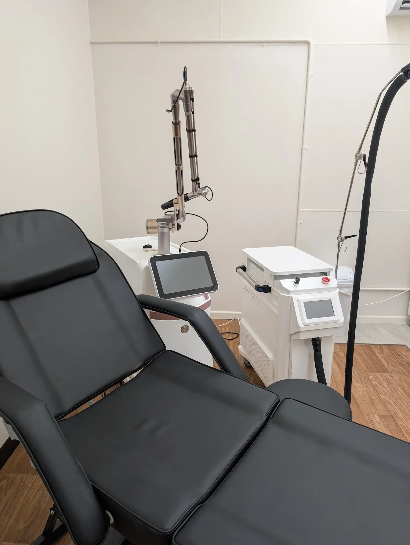 Medical examination room with a black reclining chair, medical equipment, and a white wall.