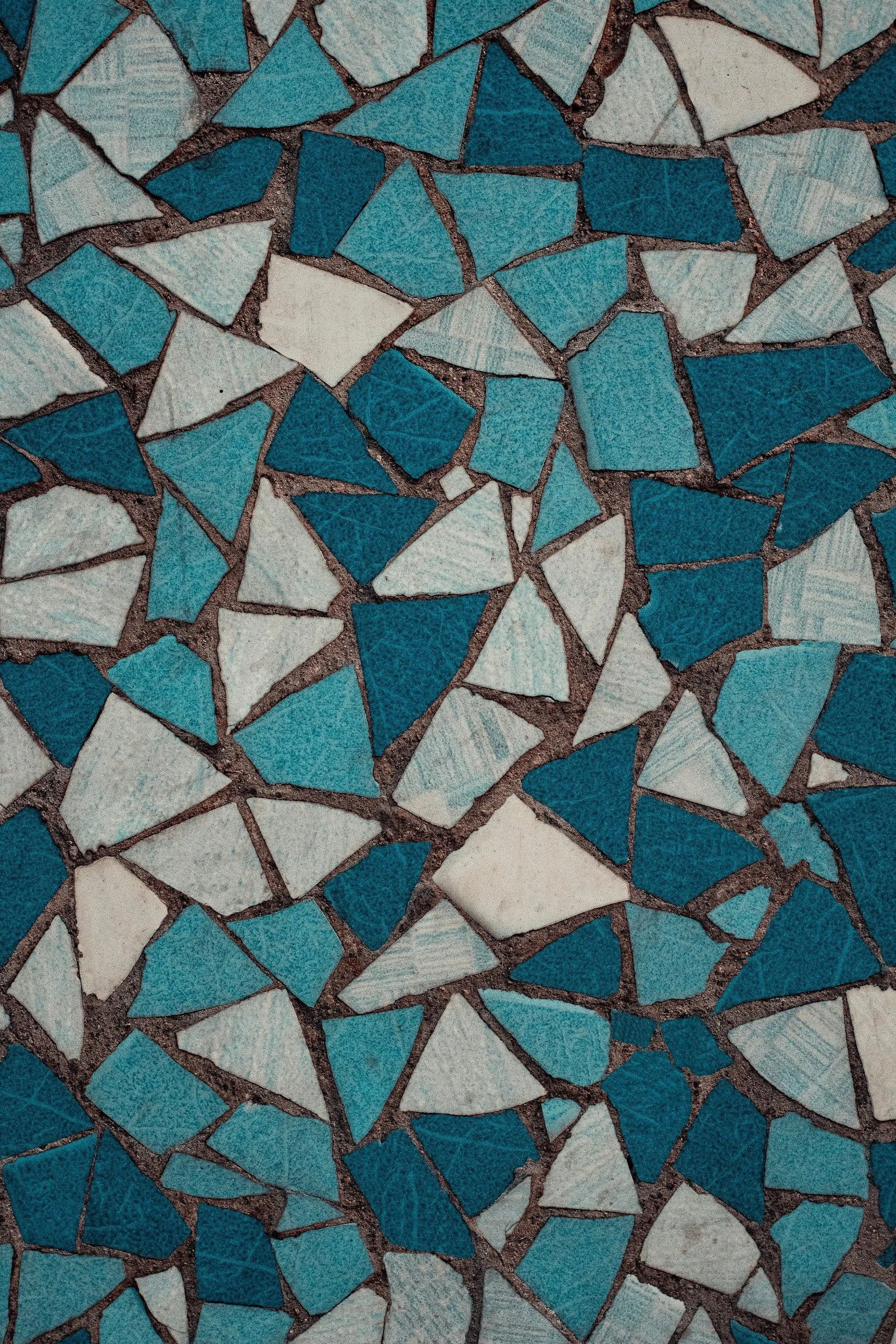 Close-up of a mosaic floor made of blue and white ceramic tiles arranged in irregular shapes, separated by dark grout lines.