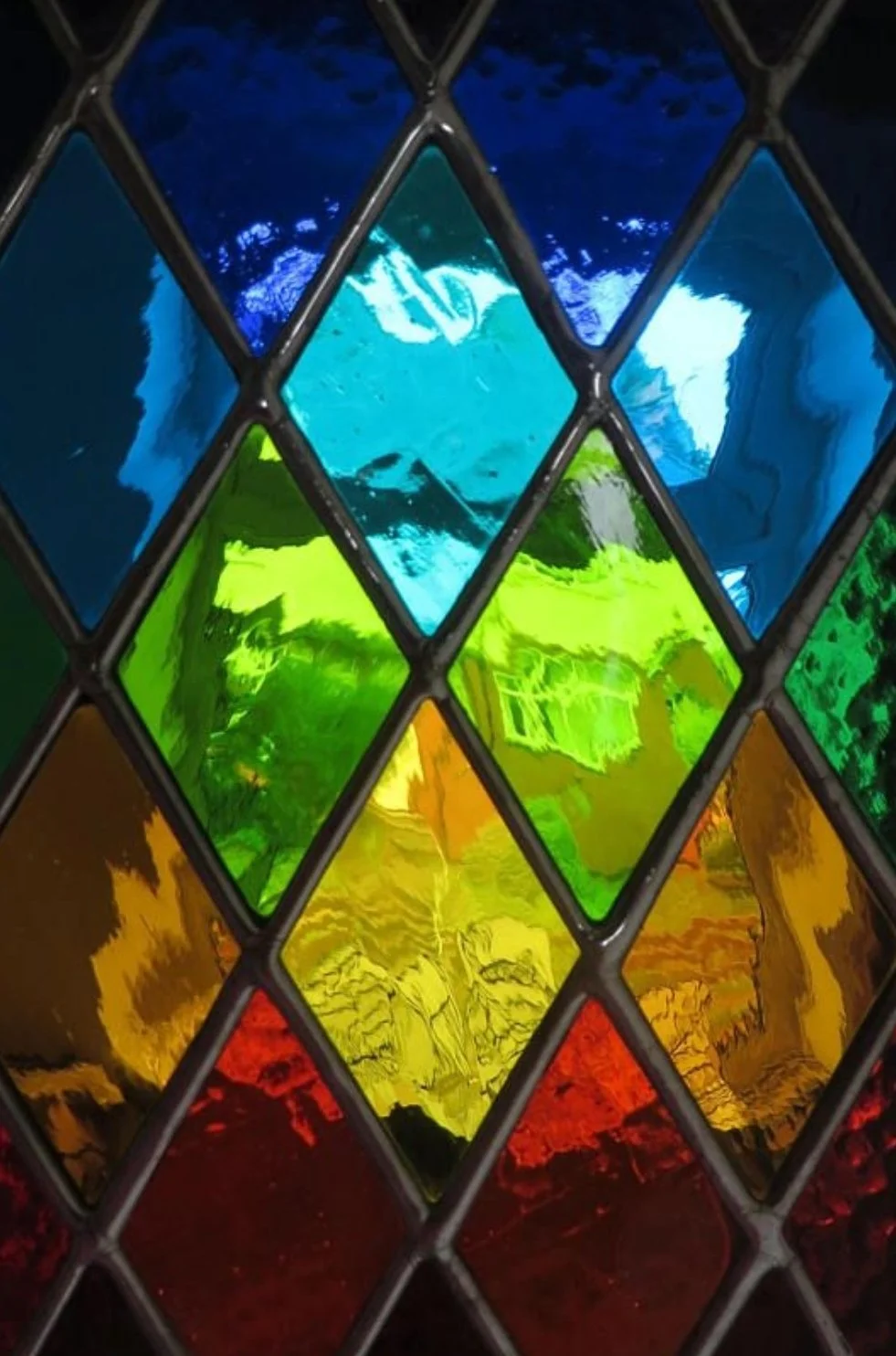 Colorful stained glass window with sections in blue, green, yellow, orange, and red, separated by black lead frames.