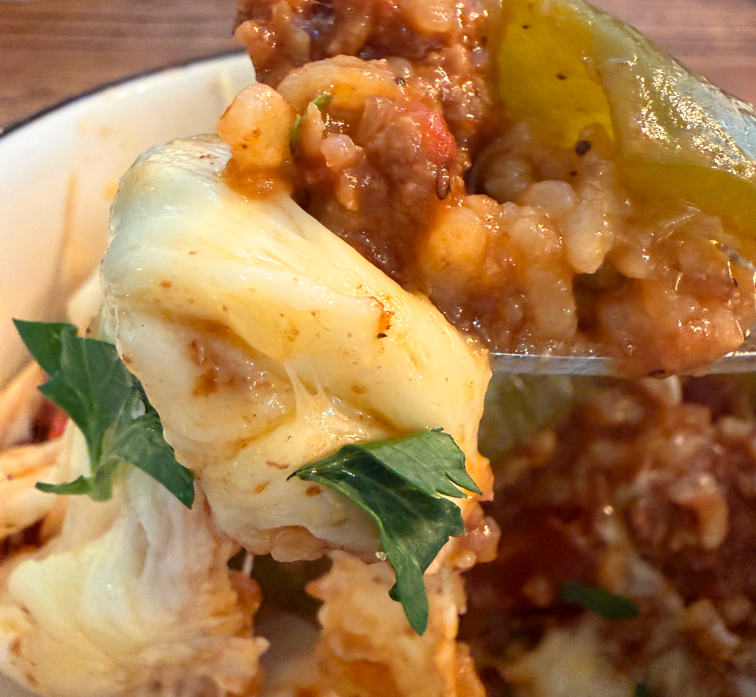 Close-up of melted cheese, ground meat, and green herbs on a slice of baked pasta or casserole dish.