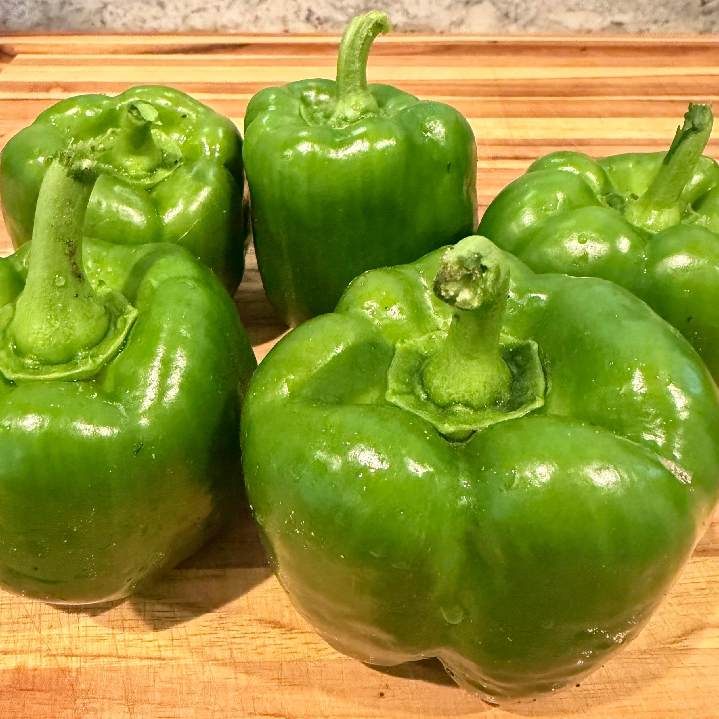 Group of fresh green bell peppers on a wooden surface.