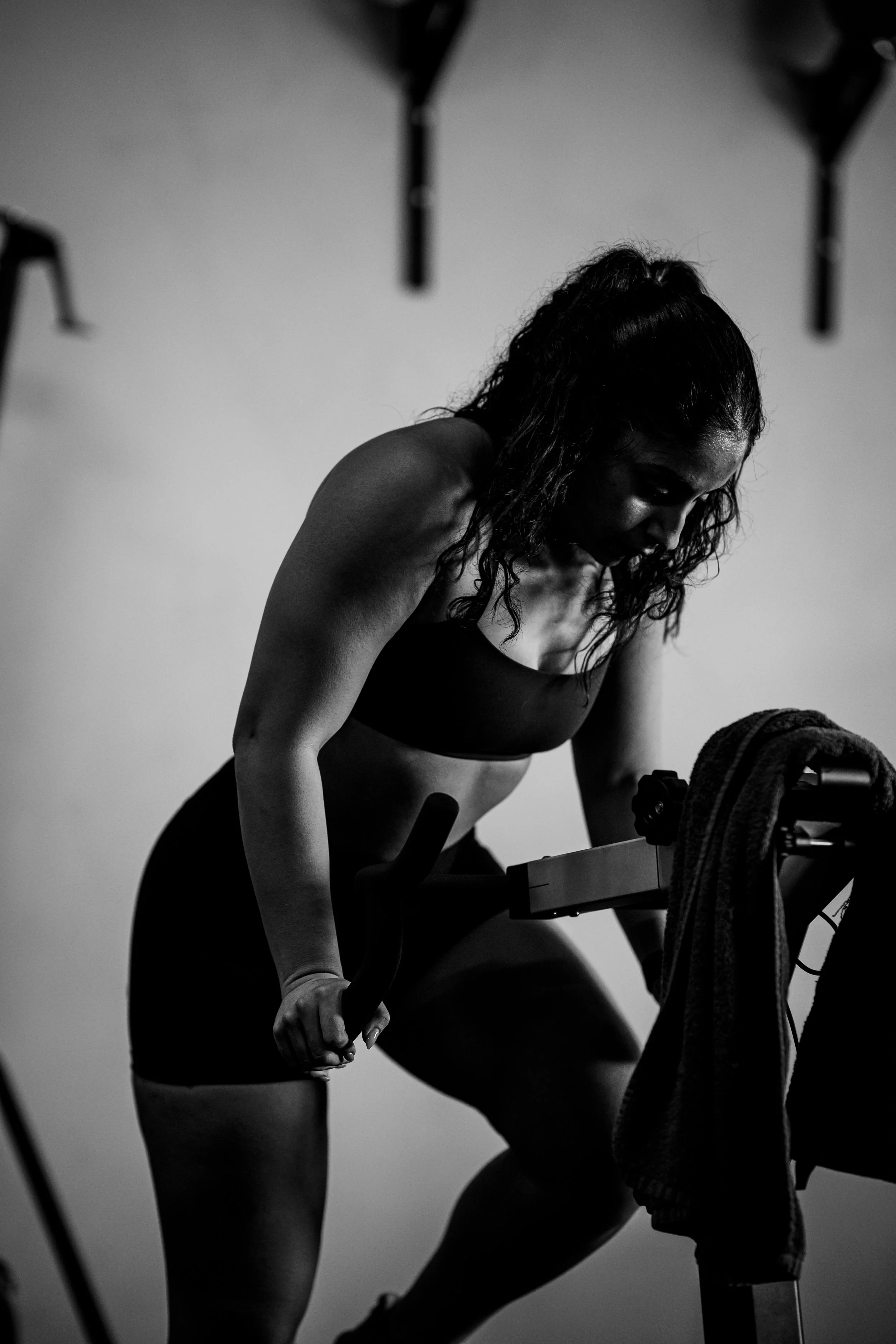 A woman with curly hair in workout clothes cycling on a bike in a gym at Train Gym, Gregory Hills