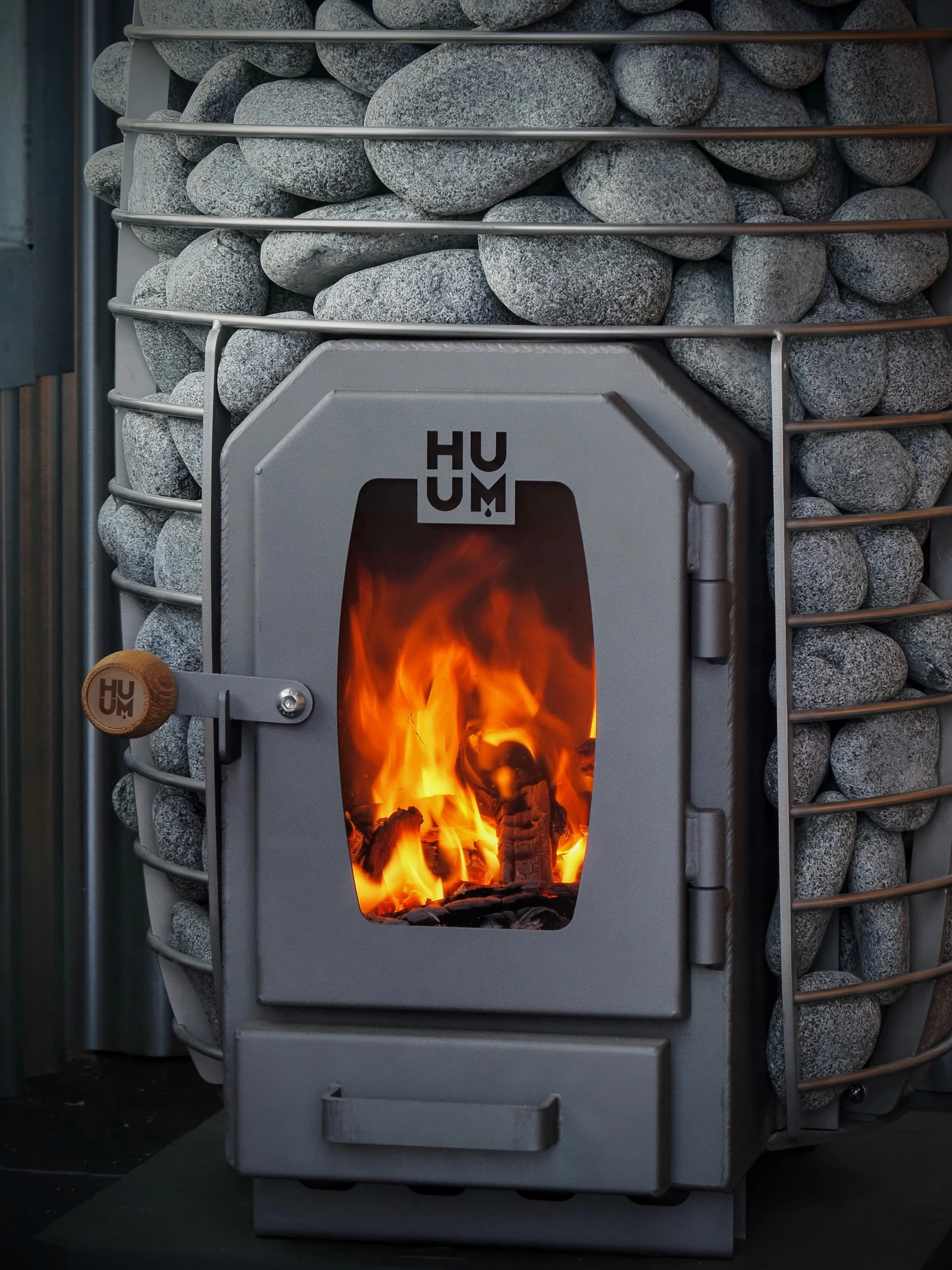 A wood-burning stove with a fire burning inside, surrounded by a metal frame and gray stones.