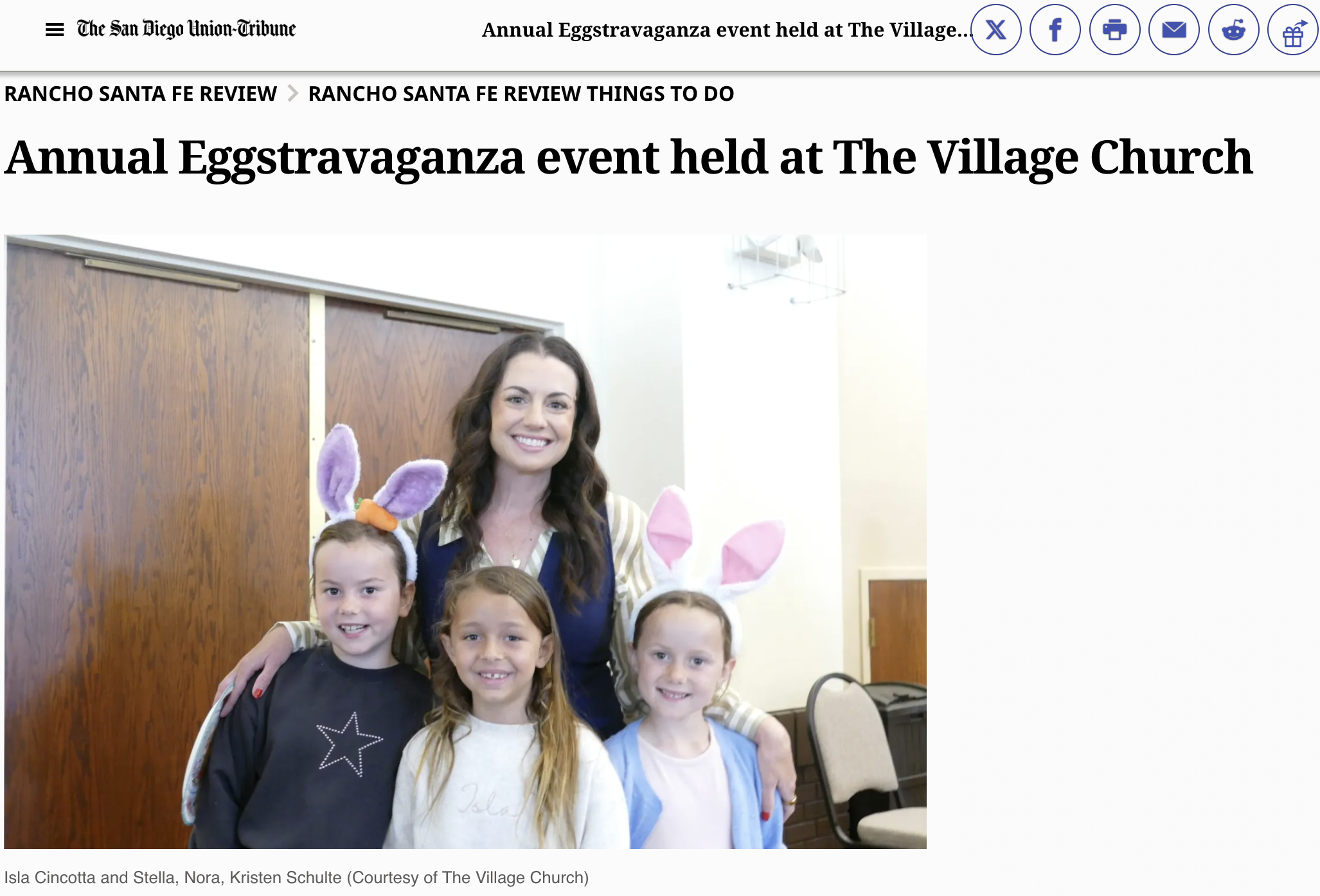 A group of children and a woman, some wearing bunny ears, standing together indoors in front of a wood-paneled wall, smiling at the camera.