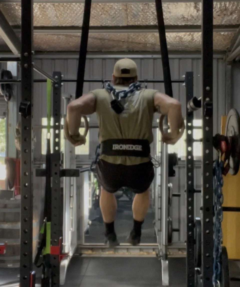 Person using a harness on a pull-up bar in a gym, with gym equipment visible around.