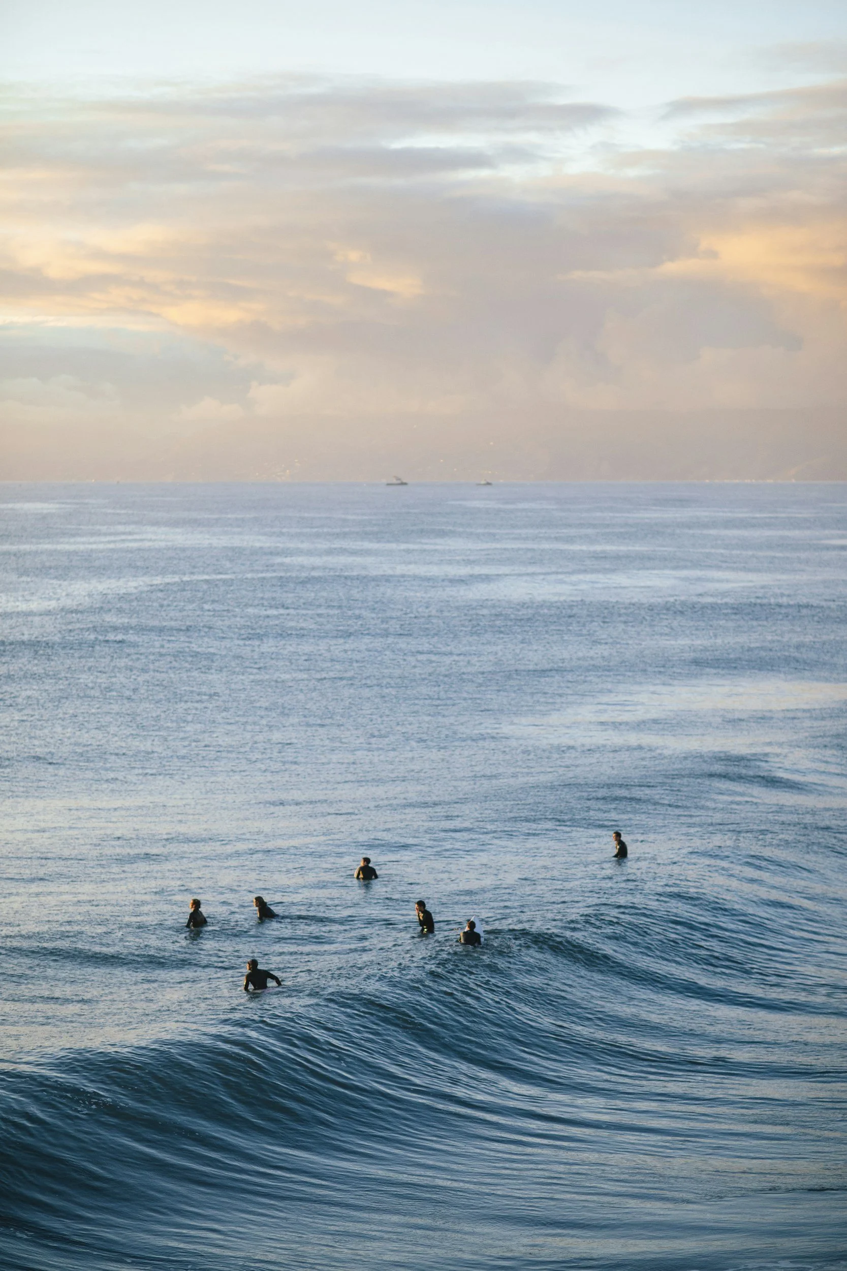 People swimming in the ocean with a cloudy sky and a distant ship or boat on the horizon.