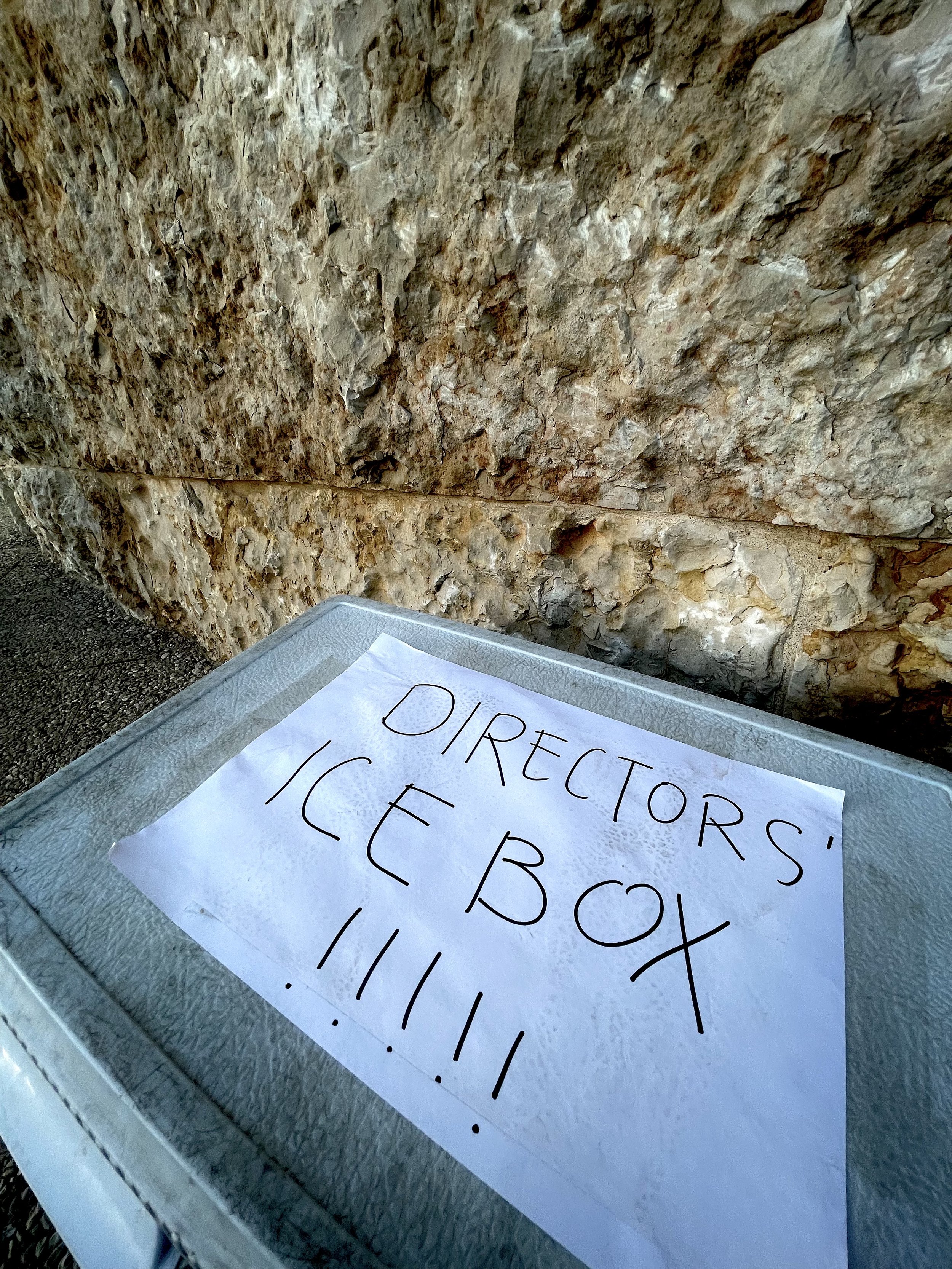 A metal tray holding a sheet of paper with handwritten instructions about an ice box, placed in front of a rough rocky wall.