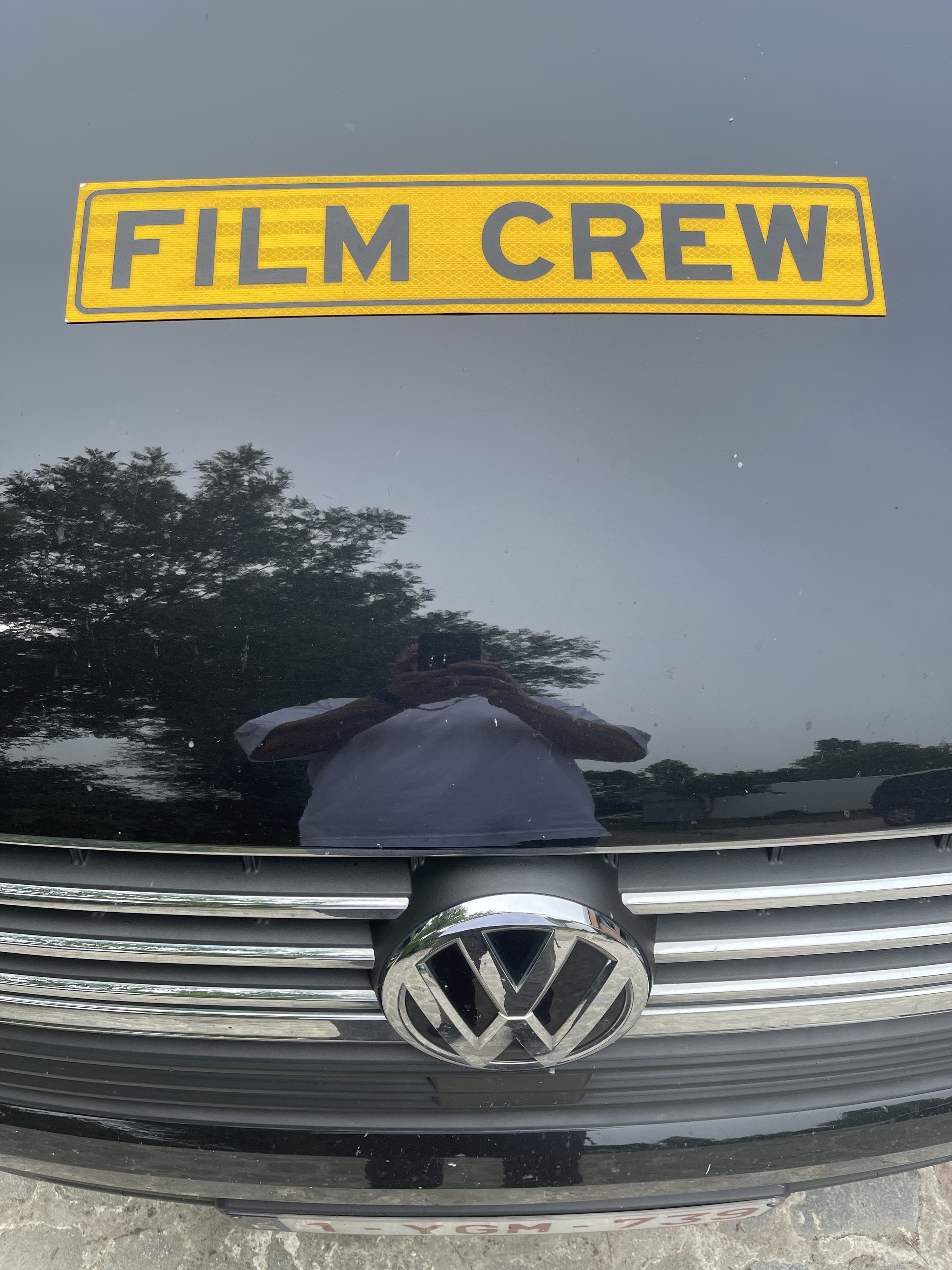 Close-up of a black Volkswagen car's front grille, with the Volkswagen logo and a yellow sticker on the hood that reads 'FILM CREW.'
