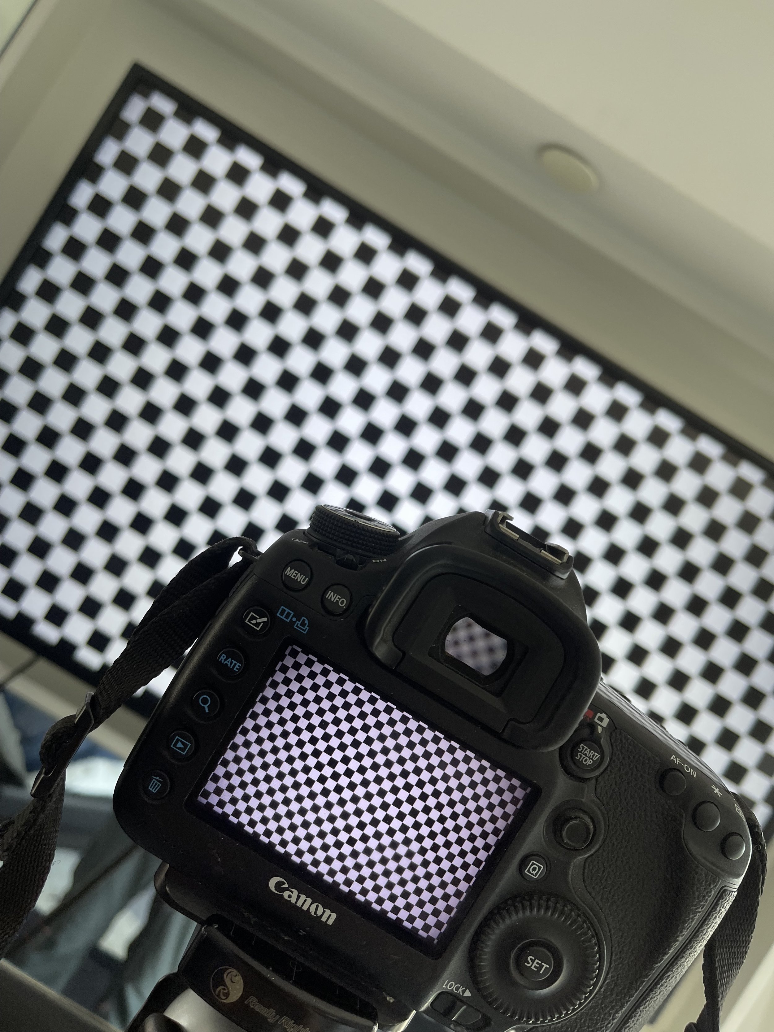 Digital camera with a black and white checkerboard pattern on its LCD screen, pointing toward a wall with a similar checkerboard pattern.