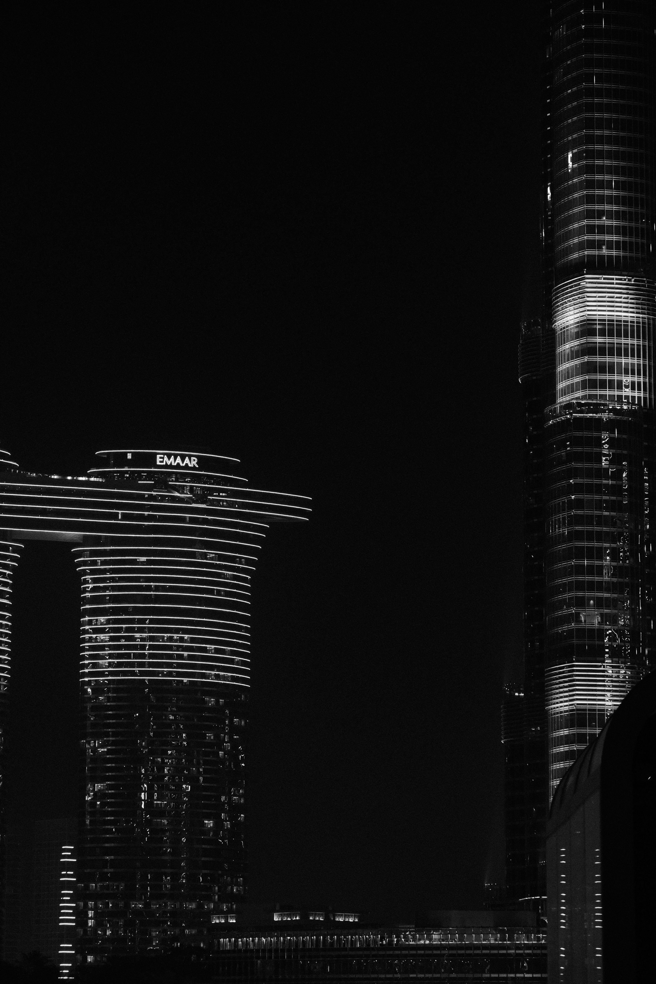 Nighttime cityscape featuring modern skyscrapers with illuminated lines outlining the buildings, including one with the logo 'Emaar' on it.