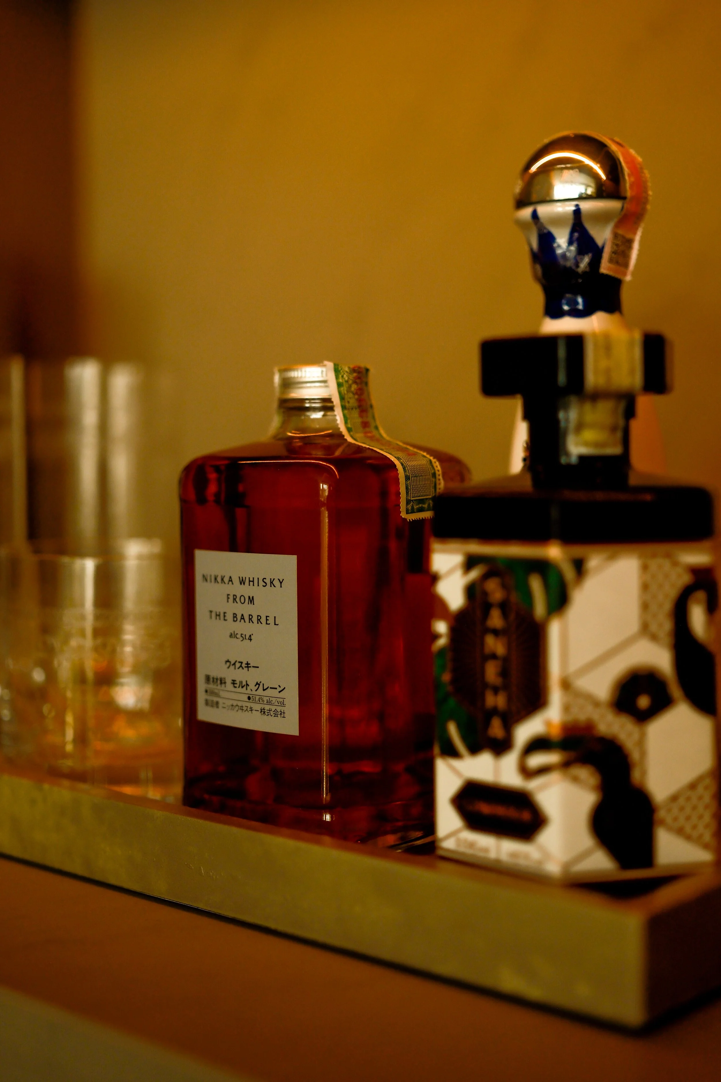 Close-up of a bottle of Nikka whisky from the barrel, with a partially visible box with bold black and white hexagonal design and a figurine with a shiny metallic head on top of it.
