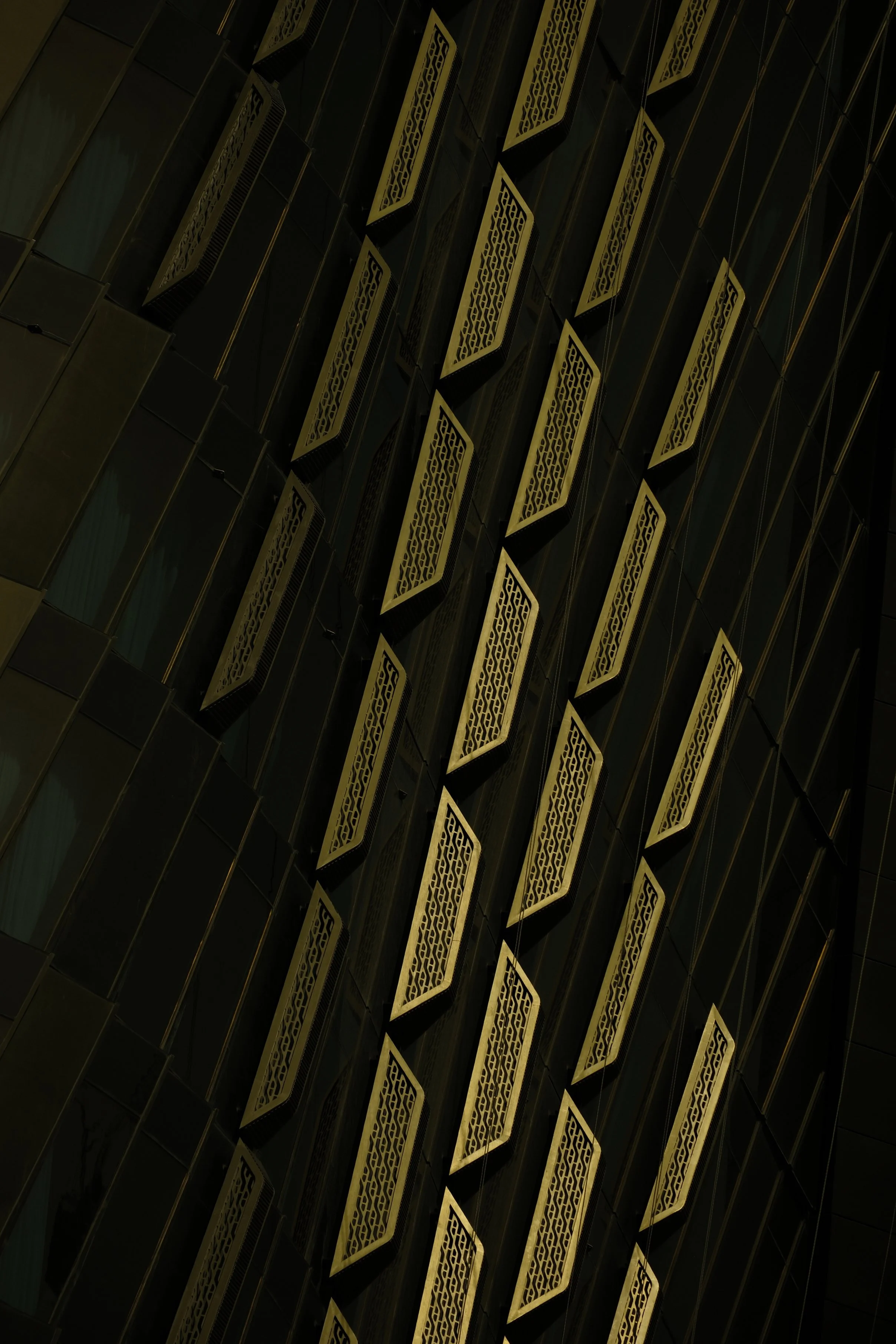 Close-up of a modern building's exterior with black glass panels and decorative golden latticework accents.