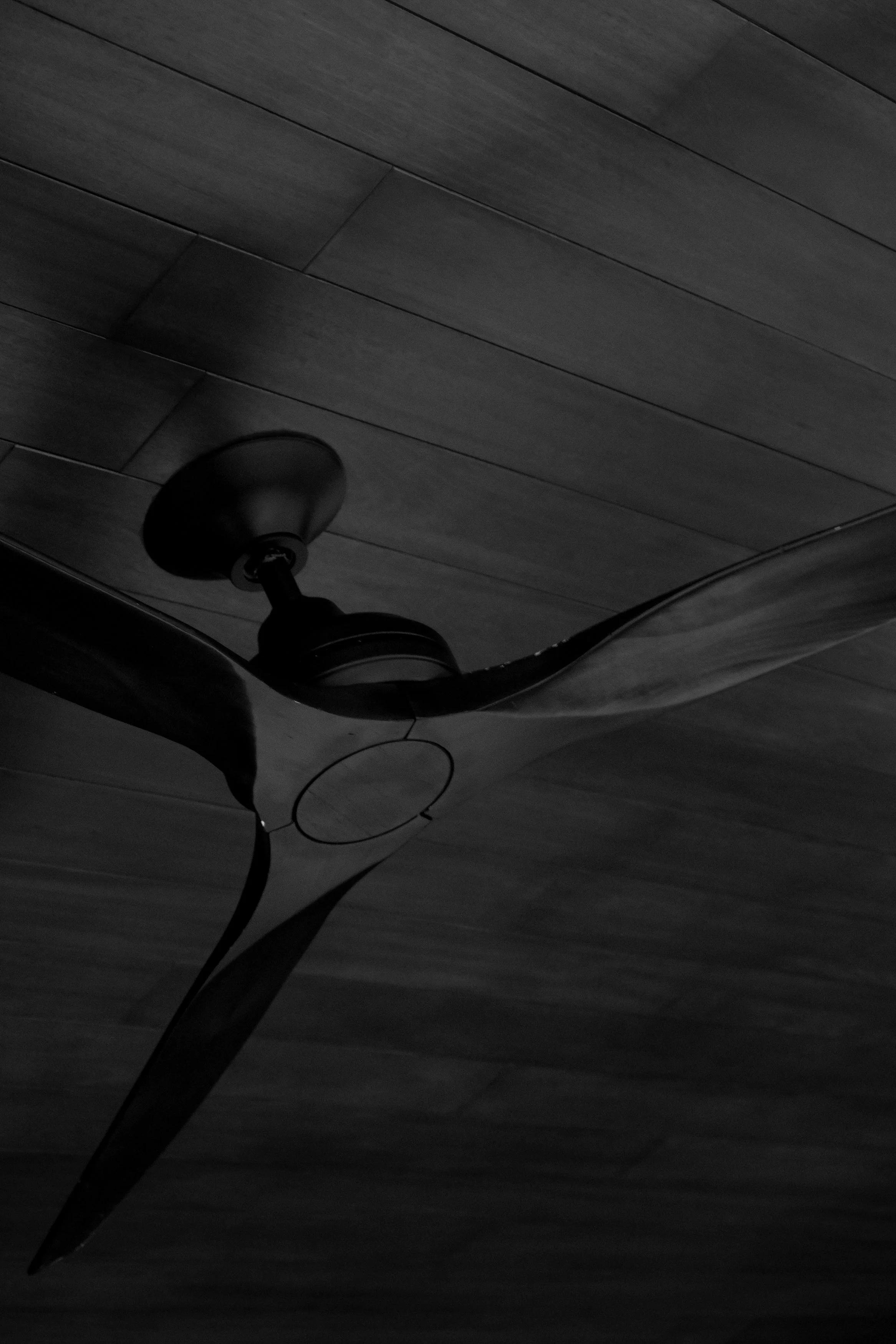 A black ceiling fan hanging from a dark wooden ceiling.