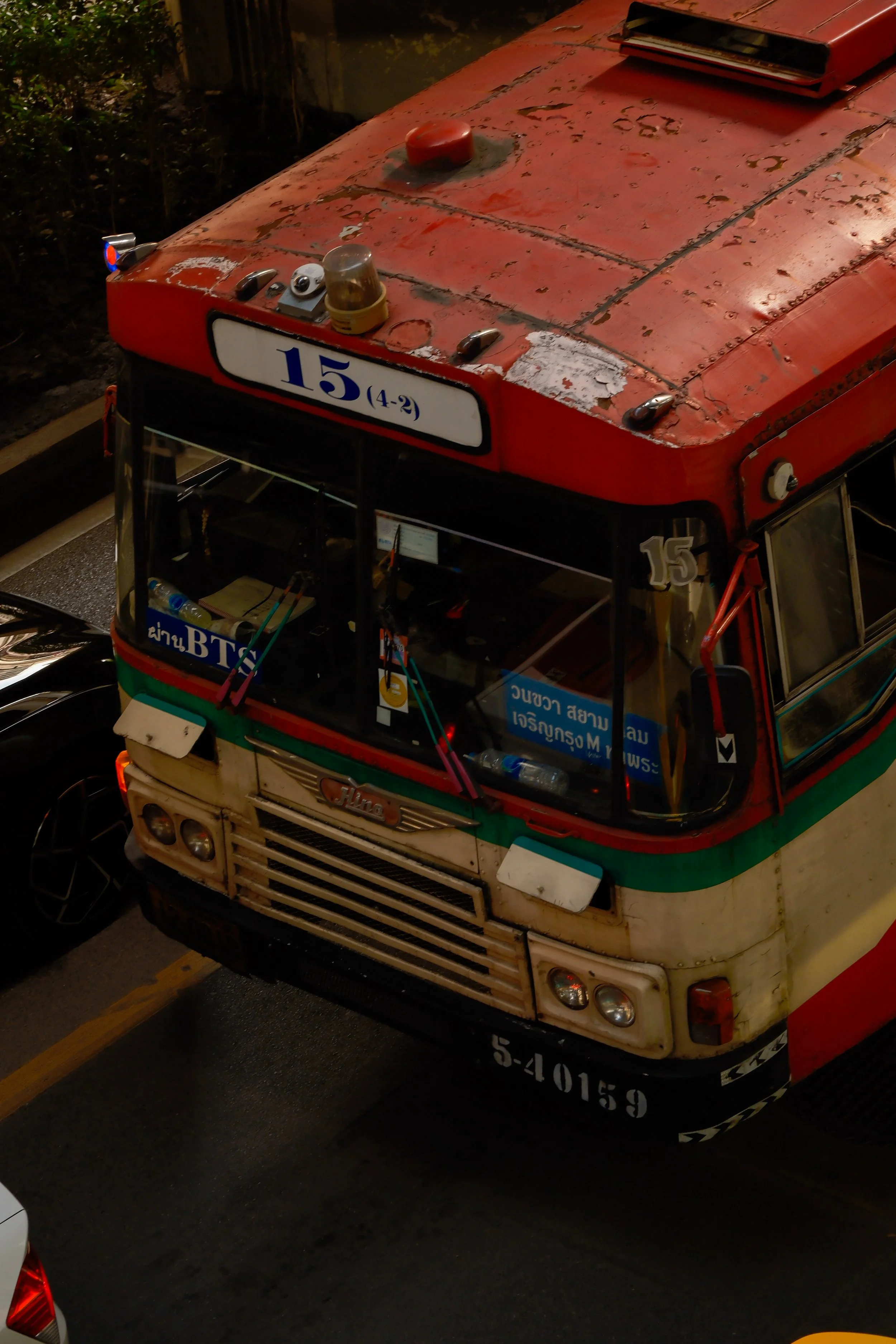 Top view of an old, weathered red and white bus with signs and equipment on the roof, including a light and a siren, on a dark street.