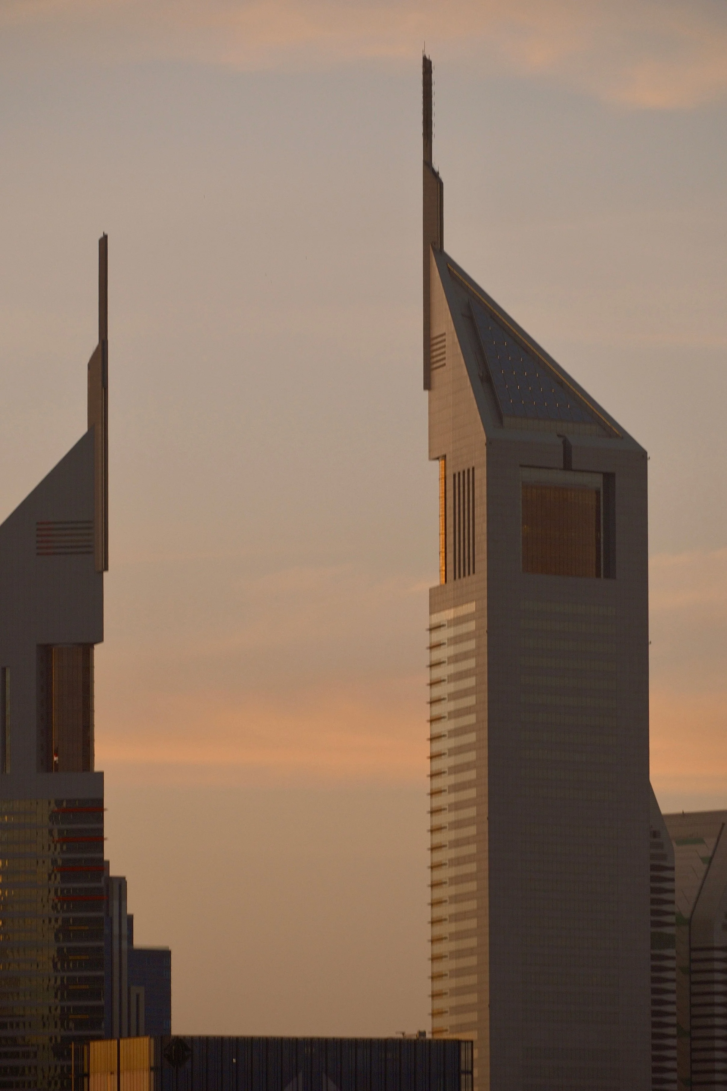 Skyline of tall modern skyscrapers during sunset with orange and pink hues in the sky.