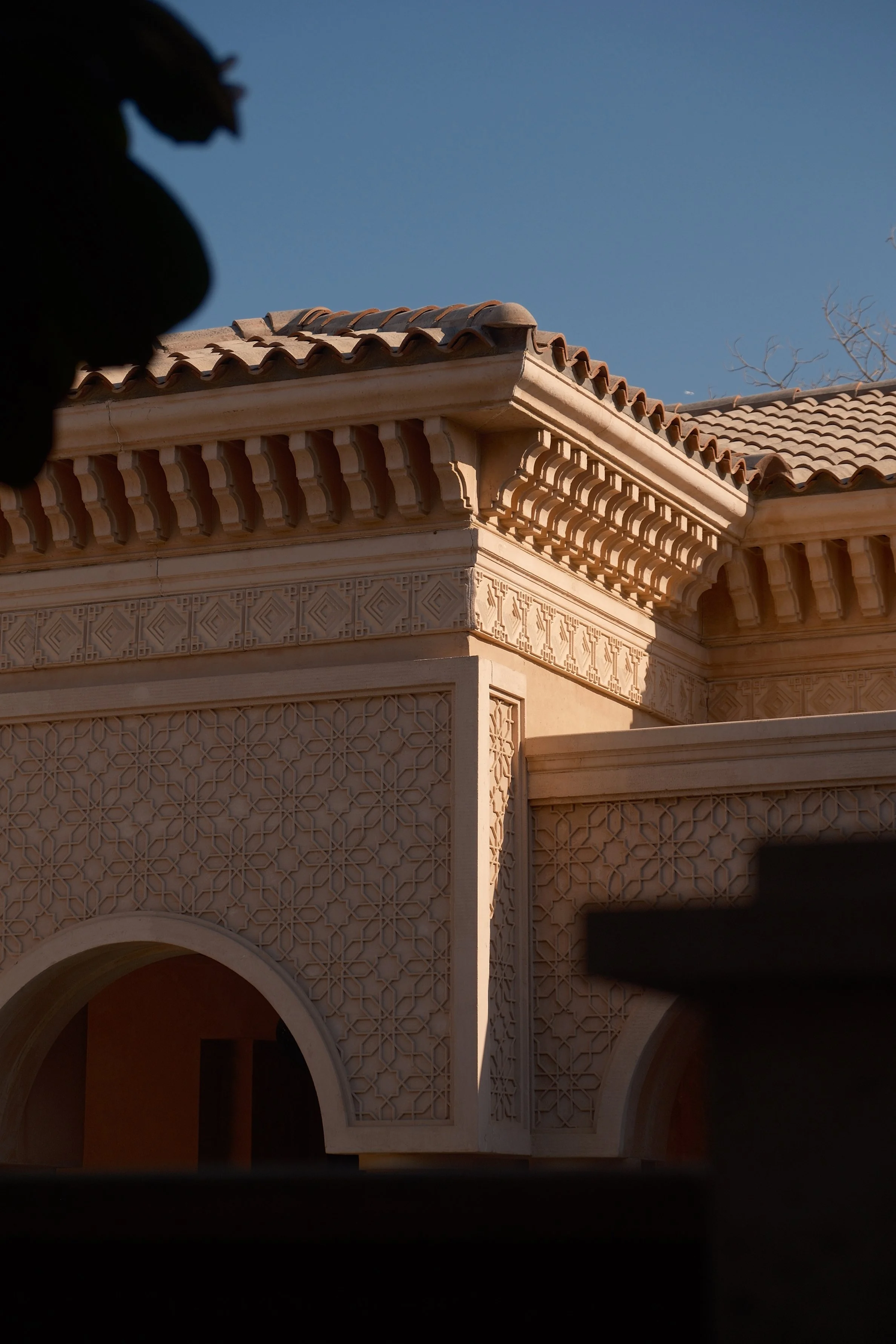 Close-up of a building with intricate geometric architectural details and terracotta roof tiles against a clear blue sky.