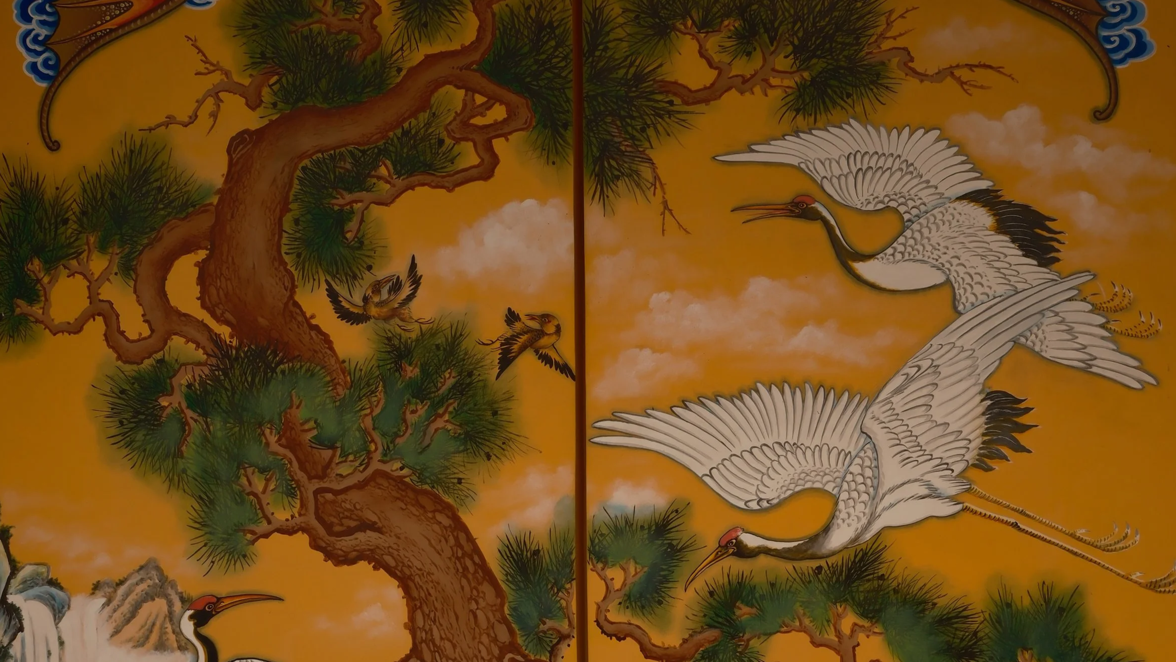 Colorful painting of cranes and birds flying near pine trees on a yellow background.