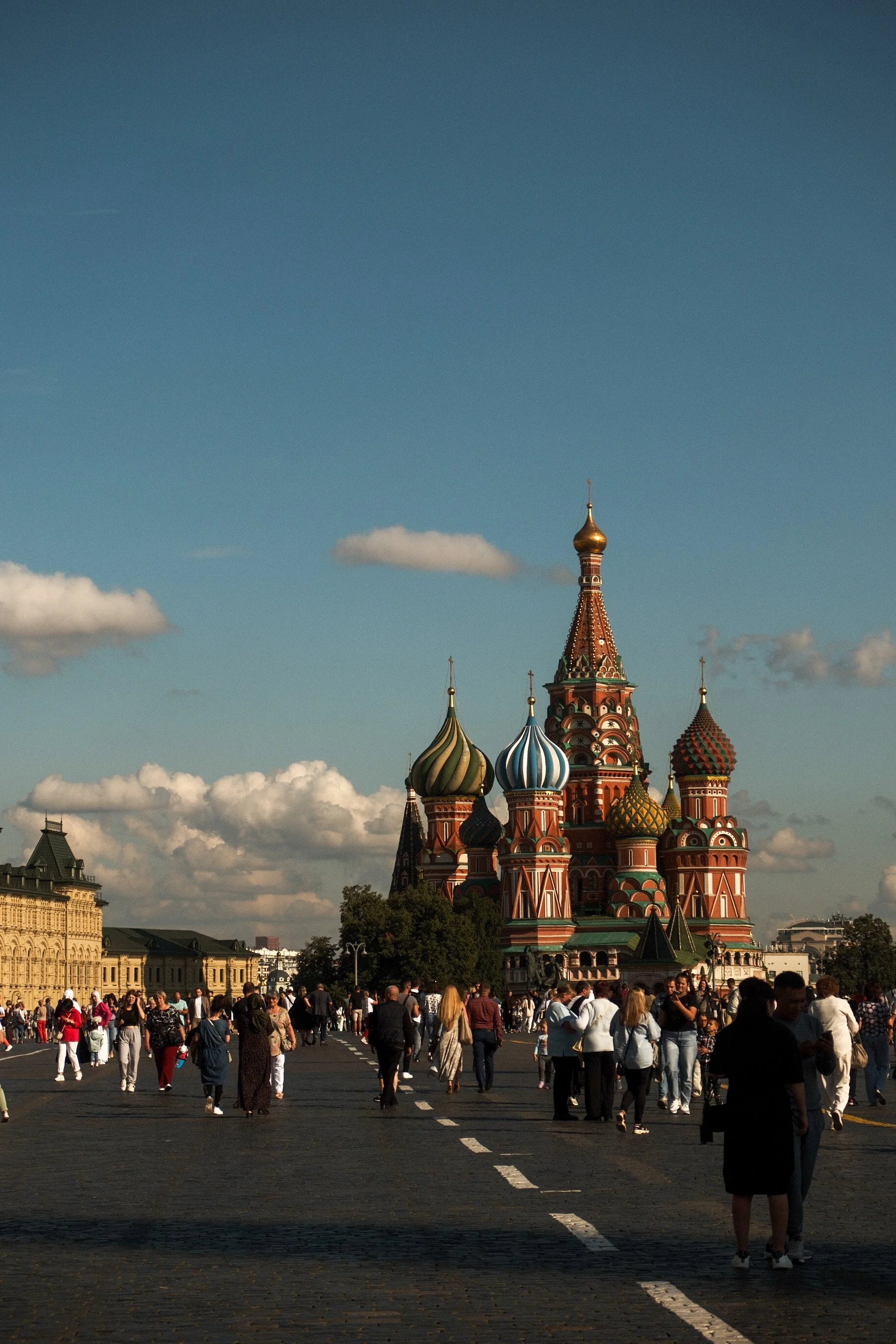 Crowd of tourists walking towards Saint Basil's Cathedral in Red Square, Moscow, with blue sky and some clouds overhead.