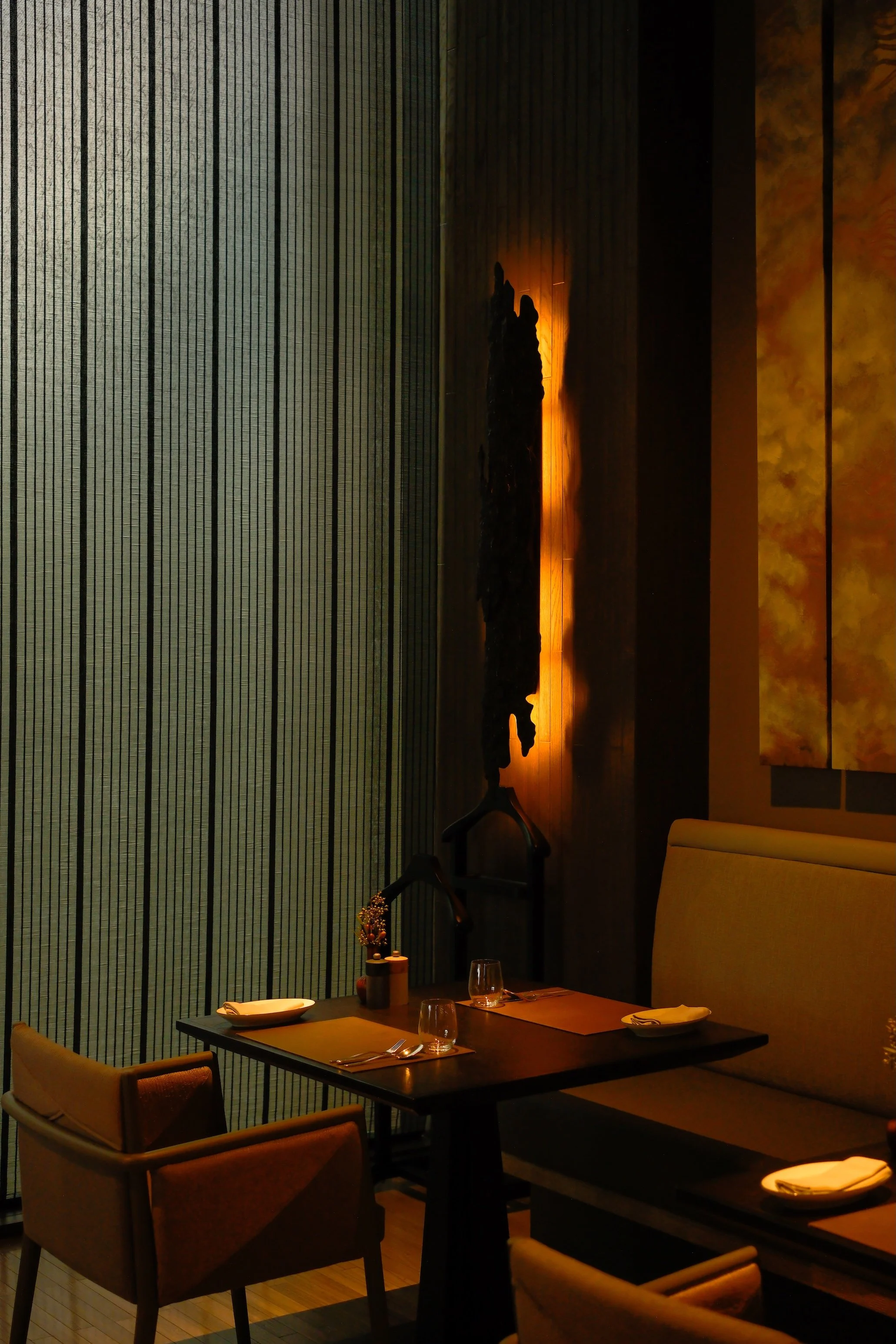 Dinner table set with plates, glasses, and cutlery in a dimly lit restaurant with modern decor and wall art.