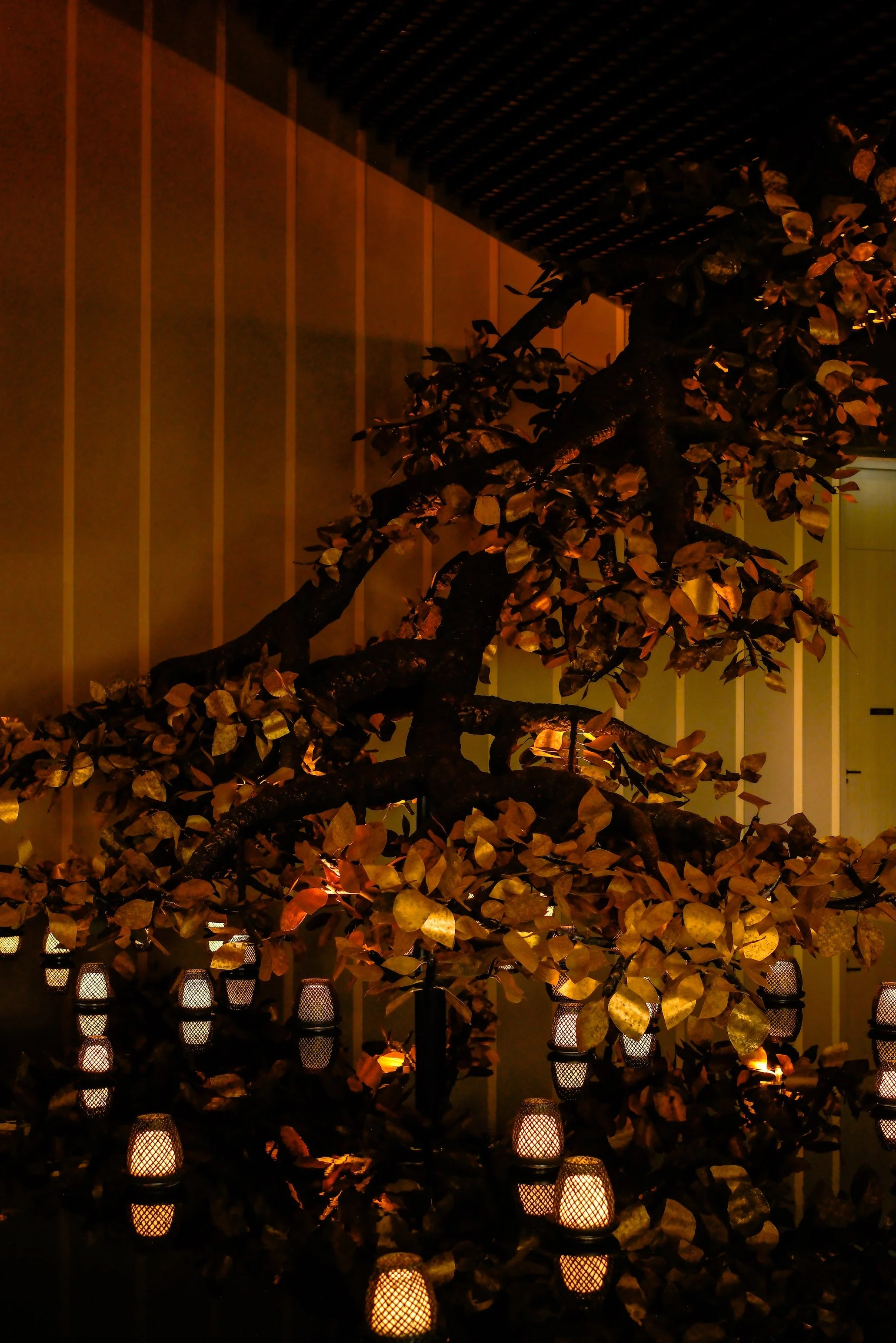 Dimly lit artificial bonsai tree surrounded by small lanterns with warm glowing lights.