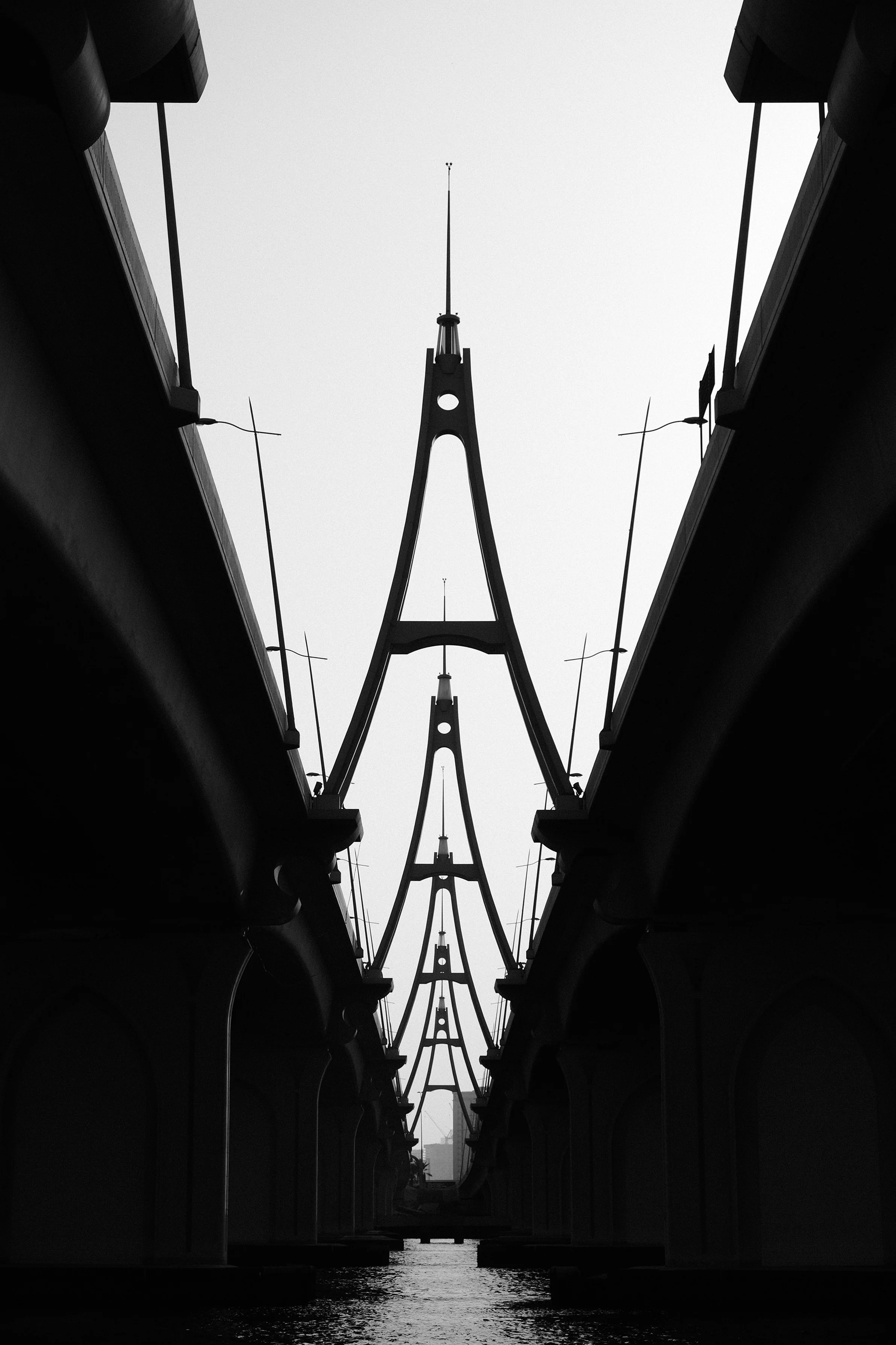 Black and white photo of a bridge taken from below, showing its arches and support structures over a waterway.
