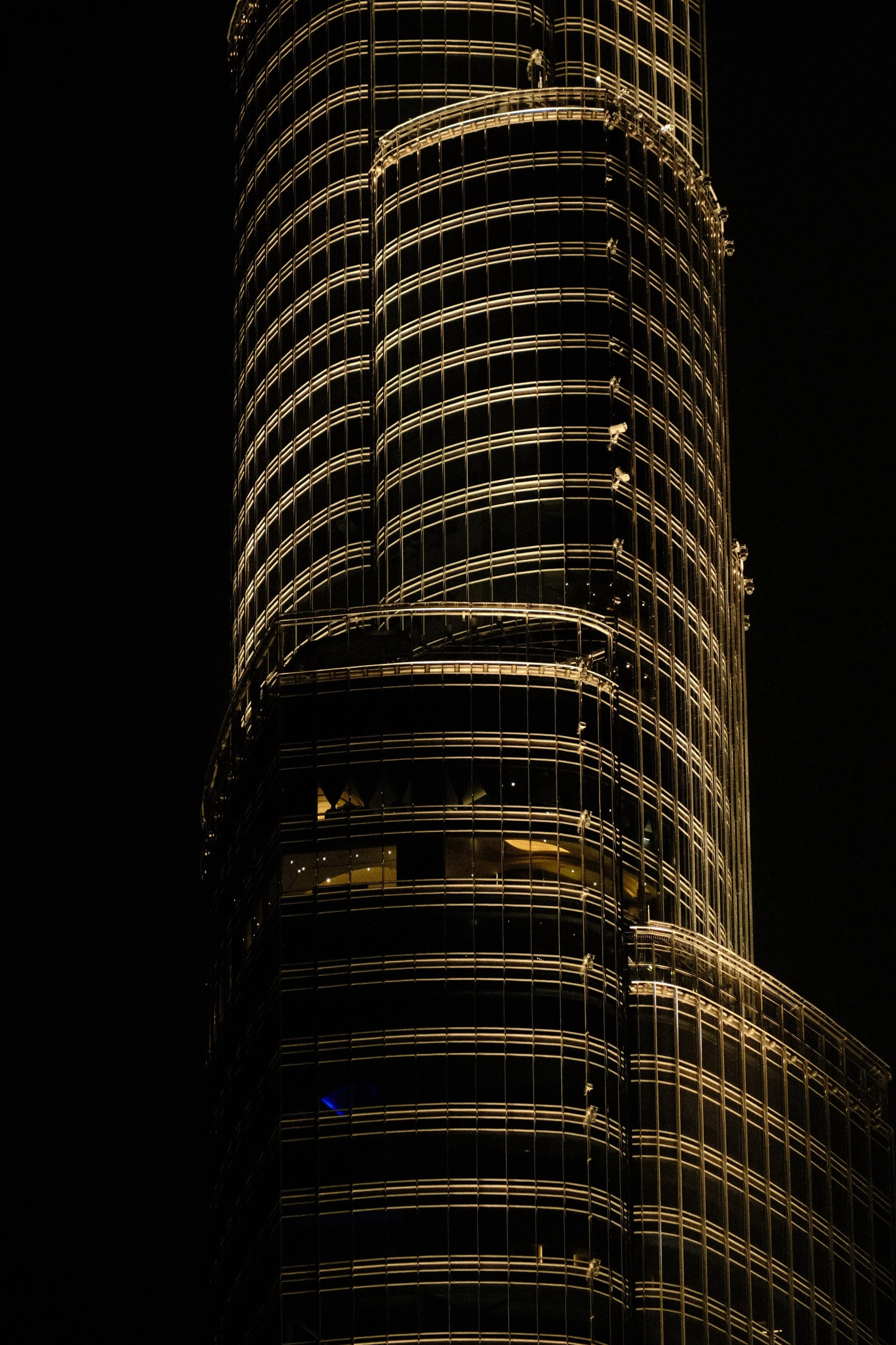 Nighttime view of a modern skyscraper with a rounded glass exterior, illuminated with warm yellow lights.