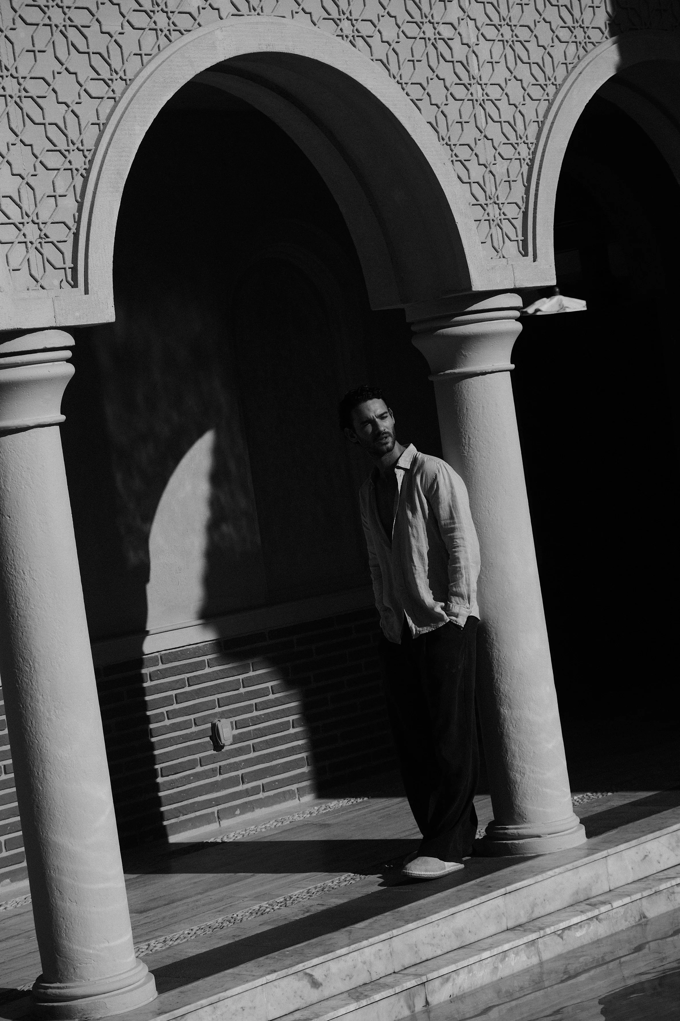 A man standing beneath an architectural archway with intricate geometric patterns in black and white.