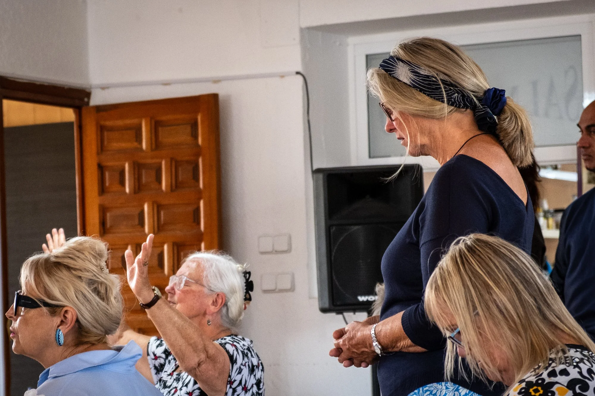 Group of older women and a woman standing and engaging in conversation at a church gathering indoors.