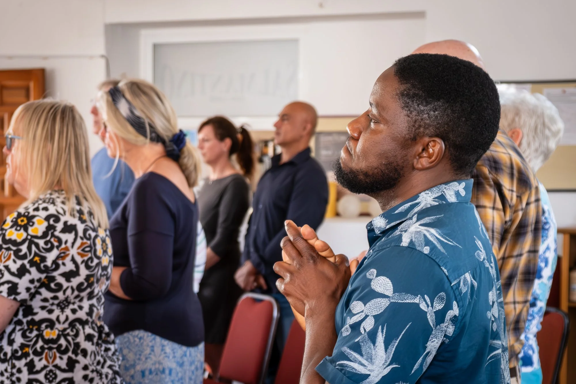 A diverse group of people seated in a church, engaging in a learning activity, with some individuals praying and others listening attentively.
