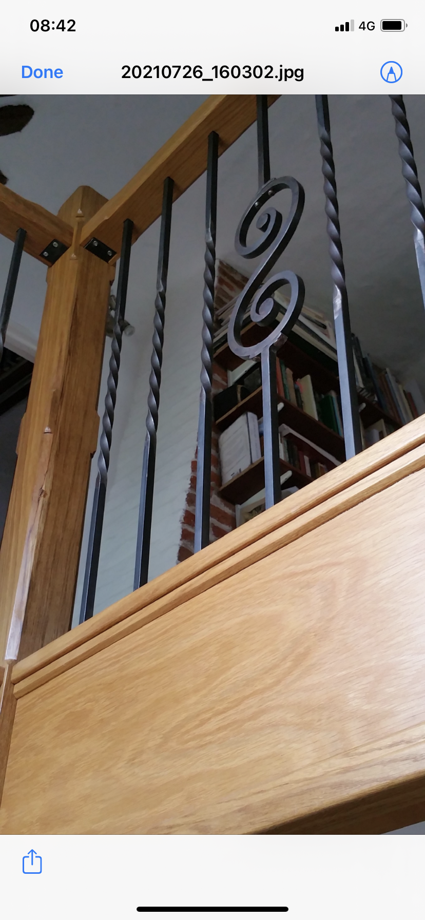 Close-up of a wooden staircase banister with decorative black metal spindles and bookshelves visible in the background.