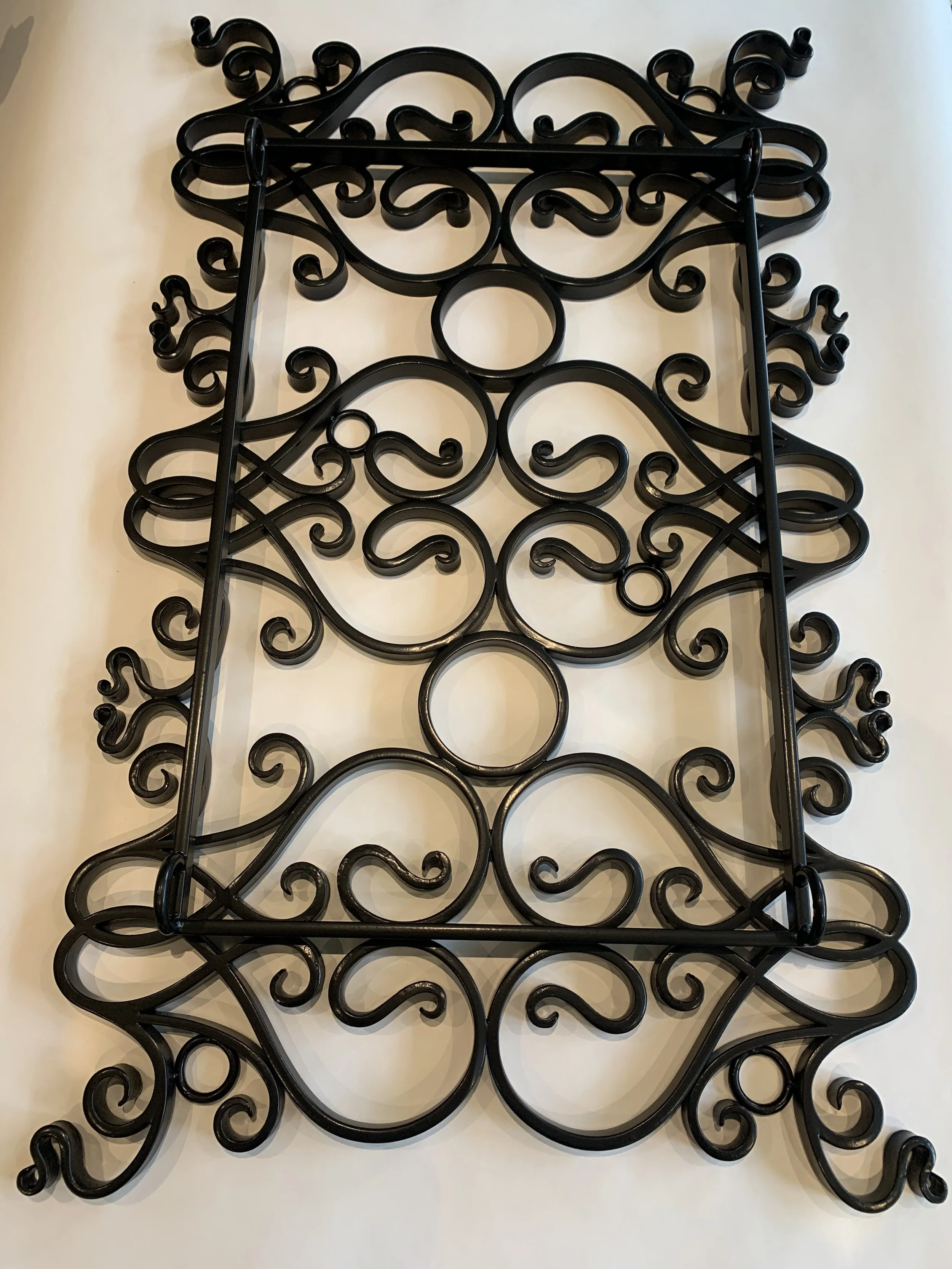 Decorative black wrought iron wall piece with intricate swirls and circular patterns, mounted on a cream-colored wall.