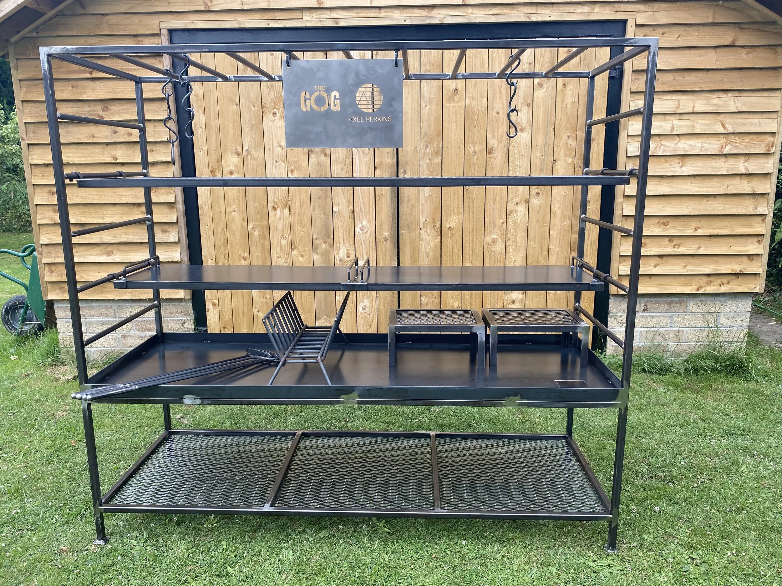 Metal outdoor fitness equipment with multiple bars and hooks in front of a wooden shed.