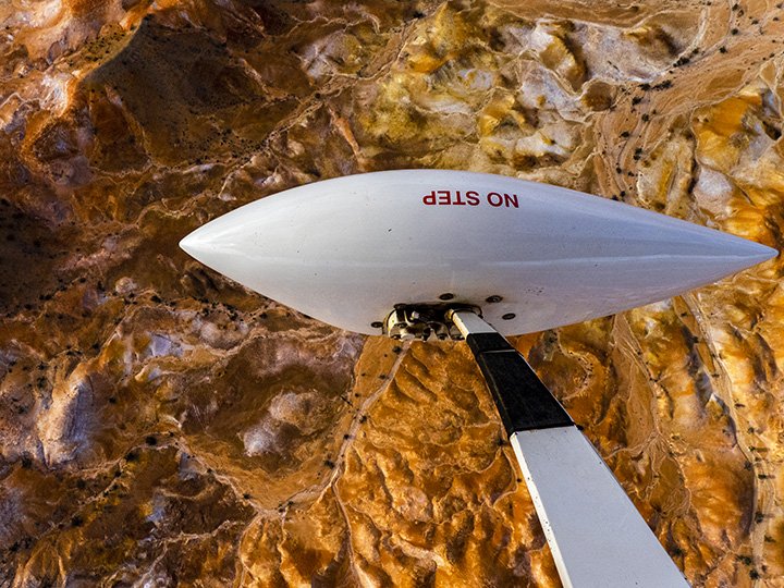 A white drone with red text that reads 'NO STEP' is mounted on a black and white aerial lift against a natural rock wall.