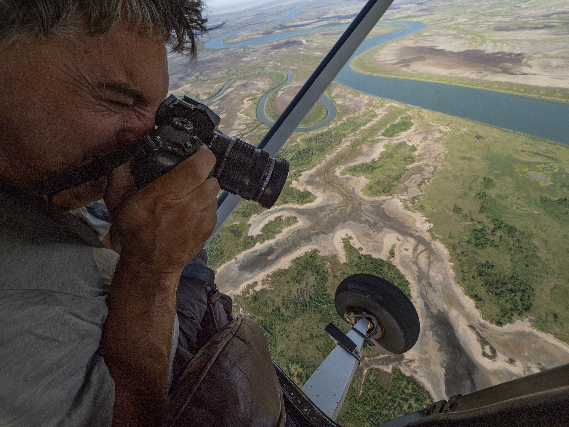 Person inside a small aircraft taking a photograph of a winding river below.