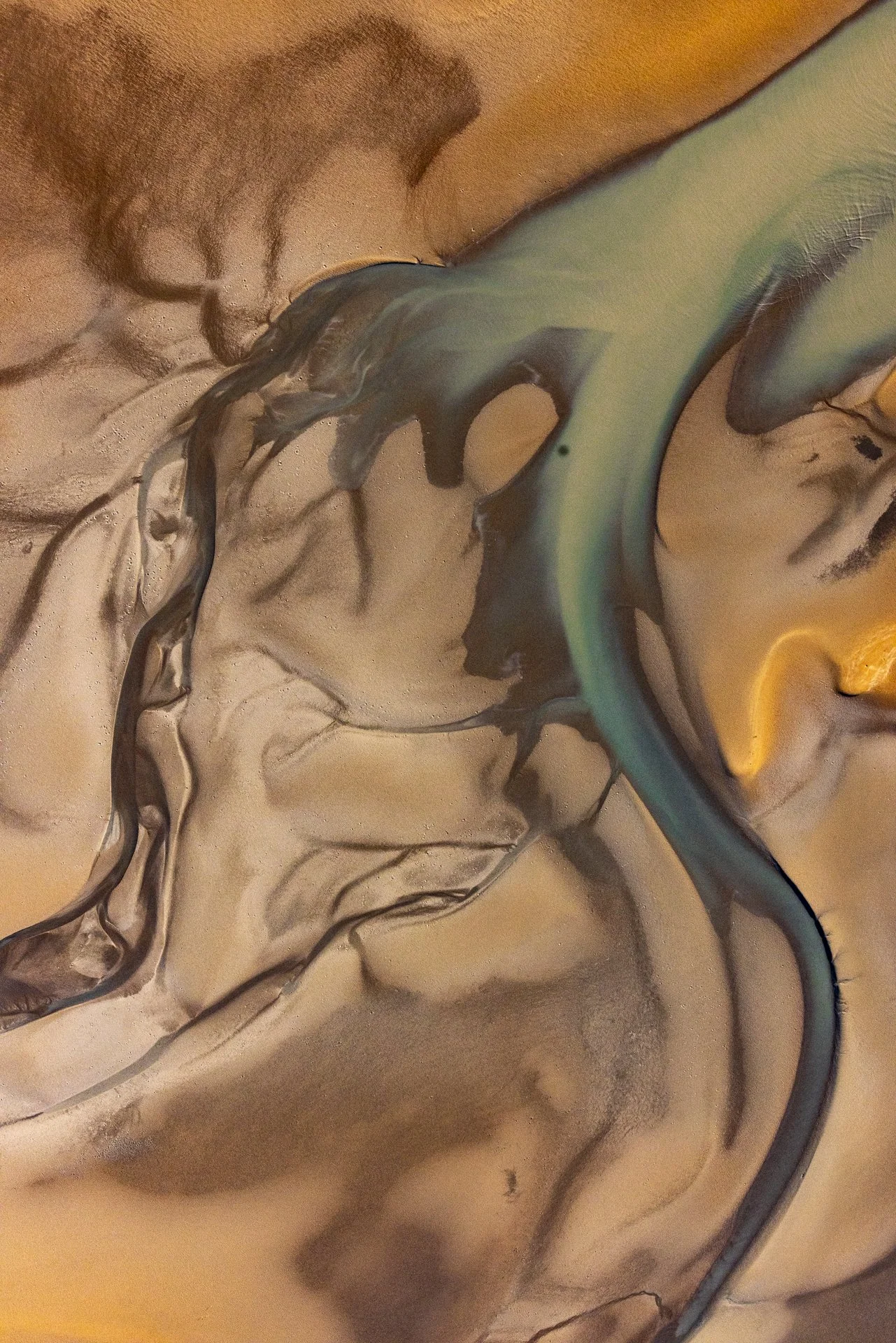Close-up of an abstract fluid painting with swirls of black, gold, and teal hues blending on a textured surface.