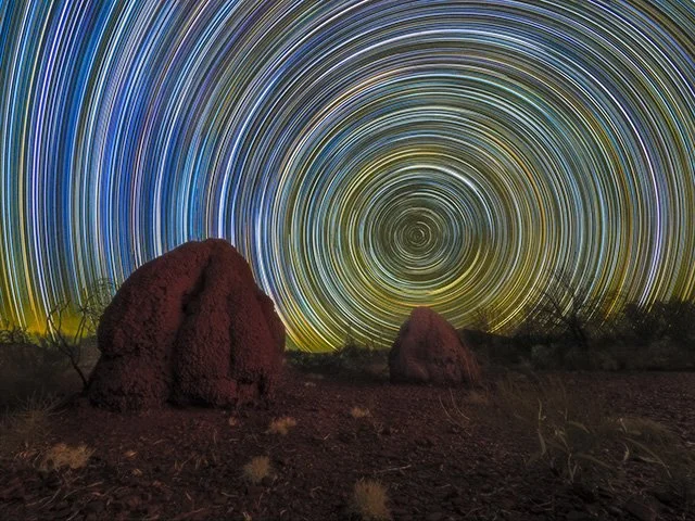 Long exposure photograph of star trails in the night sky above desert rocks.