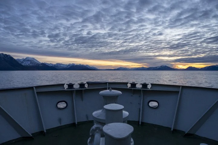 View from the expedition vessel cruising through the Arctic fjords of Northern Norway at sunset.
