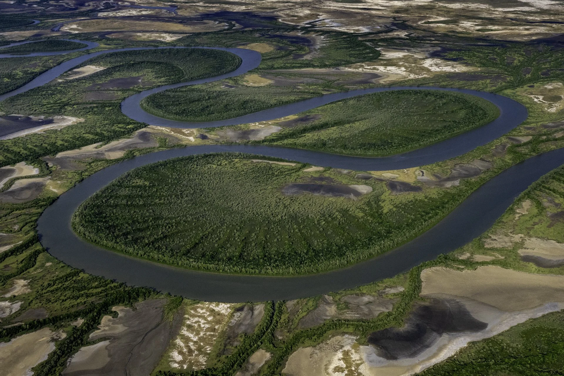 Aerial view of a winding river flowing through lush green farmland with patches of bare or harvested land.