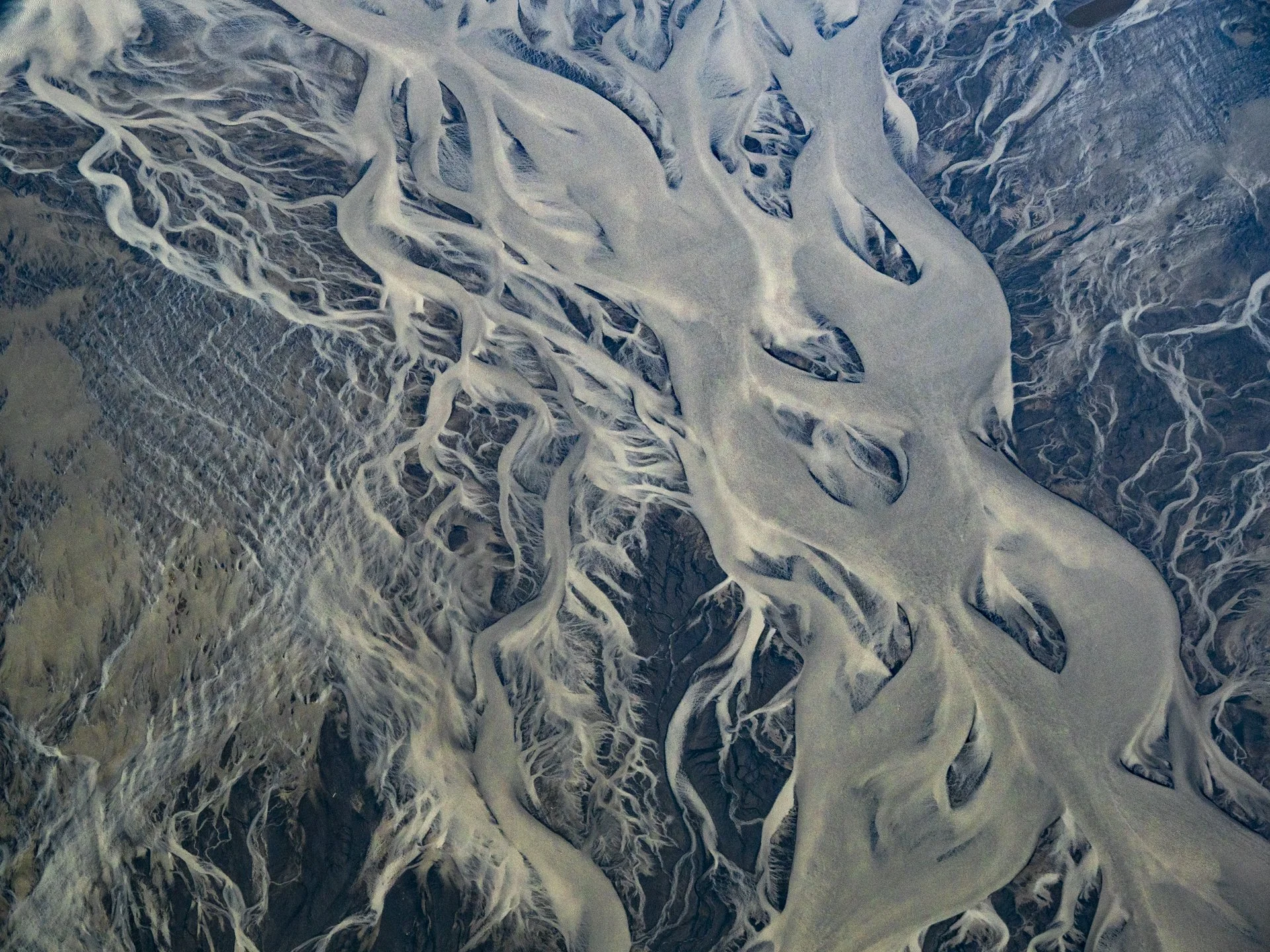 Aerial view of braided glacial rivers flowing across Iceland's volcanic landscape.