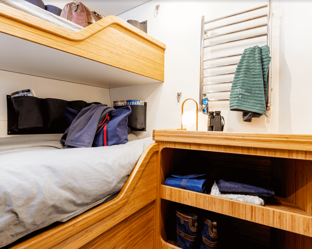 A cozy wooden bunk bed in a small room with a desk, towel rack, and various personal items and clothes.