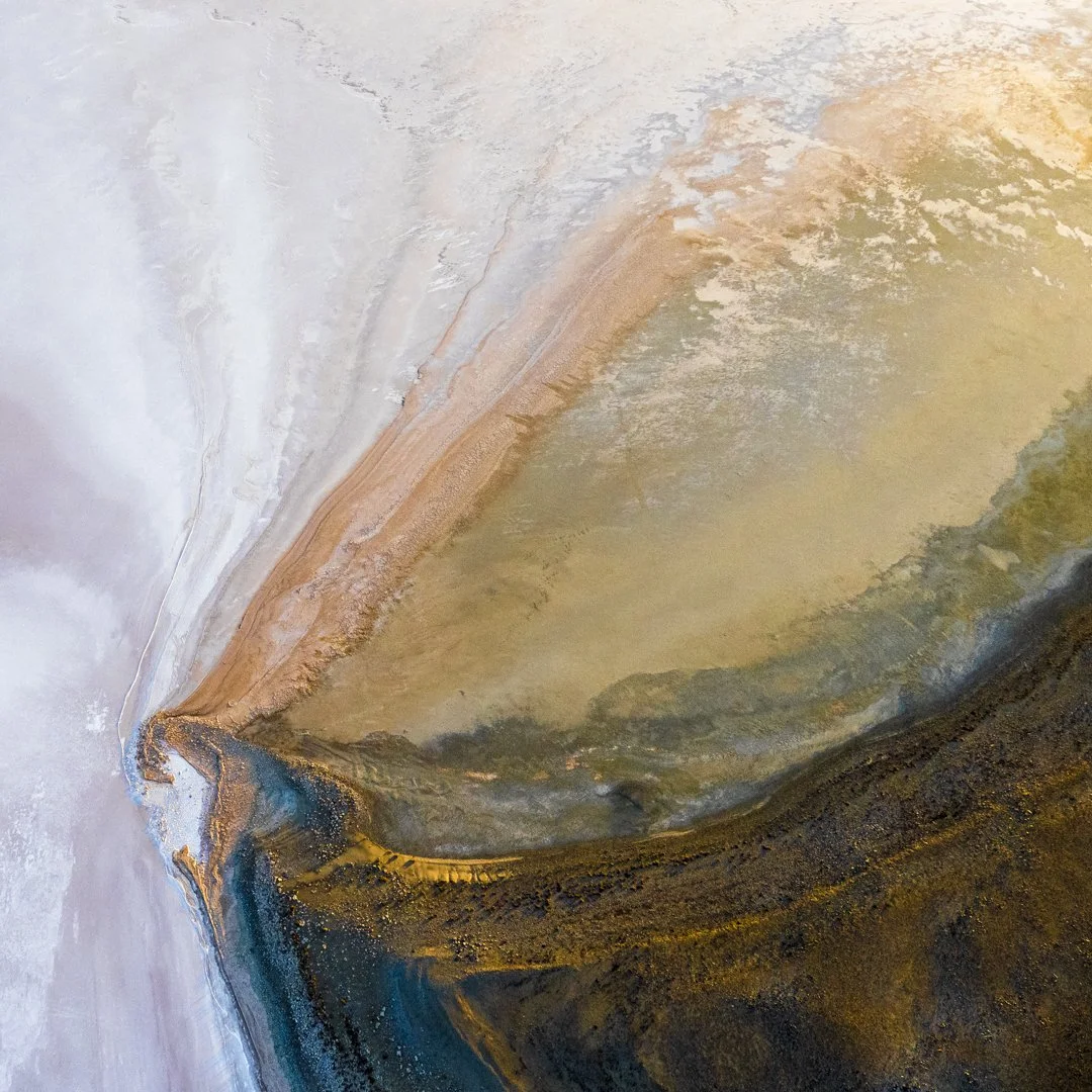 A colorful, abstract aerial view of a landscape with different textures and colors, featuring a prominent curved land formation with shades of brown, yellow, green, and dark blue.
