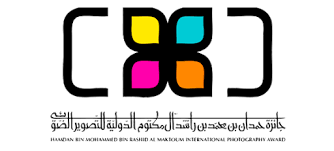 Logo featuring four colored petals in yellow, blue, pink, and orange, with surrounding black brackets and Arabic text below.